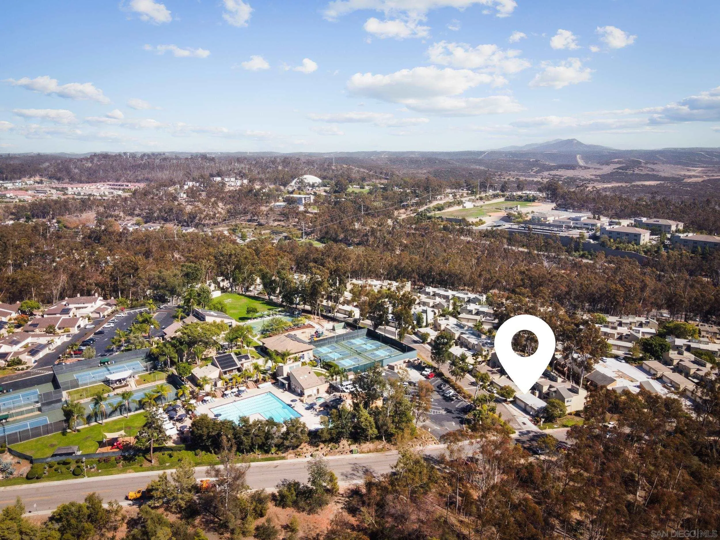 Aerial view of the residential community, with tennis courts, a swimming pool, and a location marker.