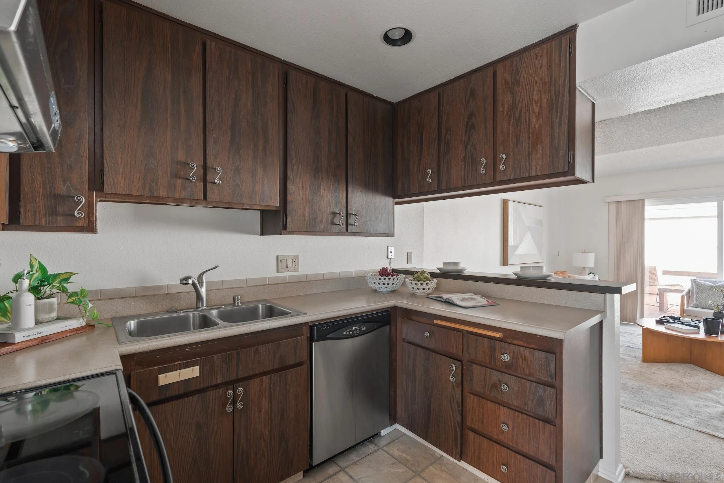 Kitchen with dark wood cabinets, double sink, and dishwasher beside a pass-through to the living room.