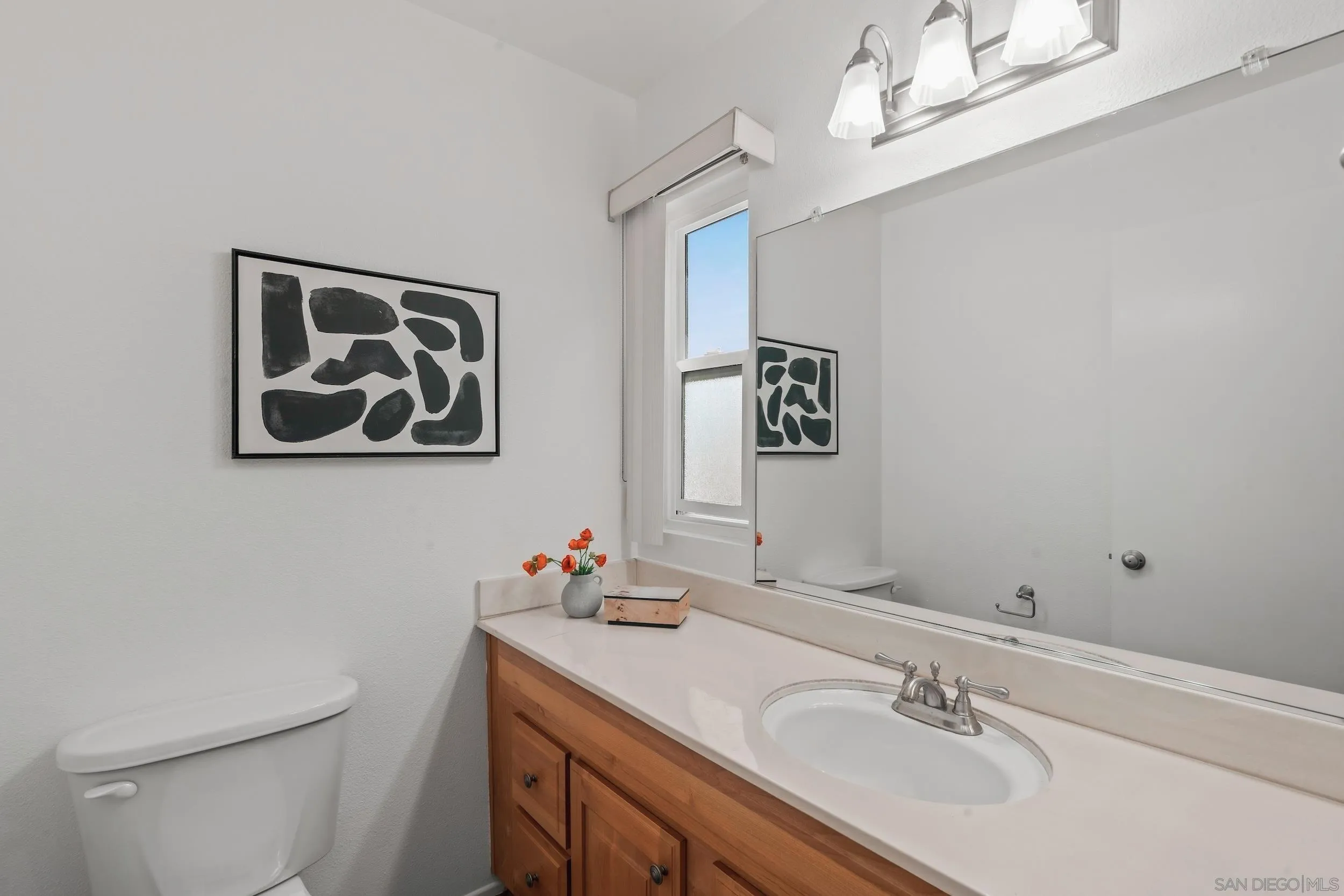 Bathroom with a wood vanity, white countertop, large mirror, and framed abstract artwork.
