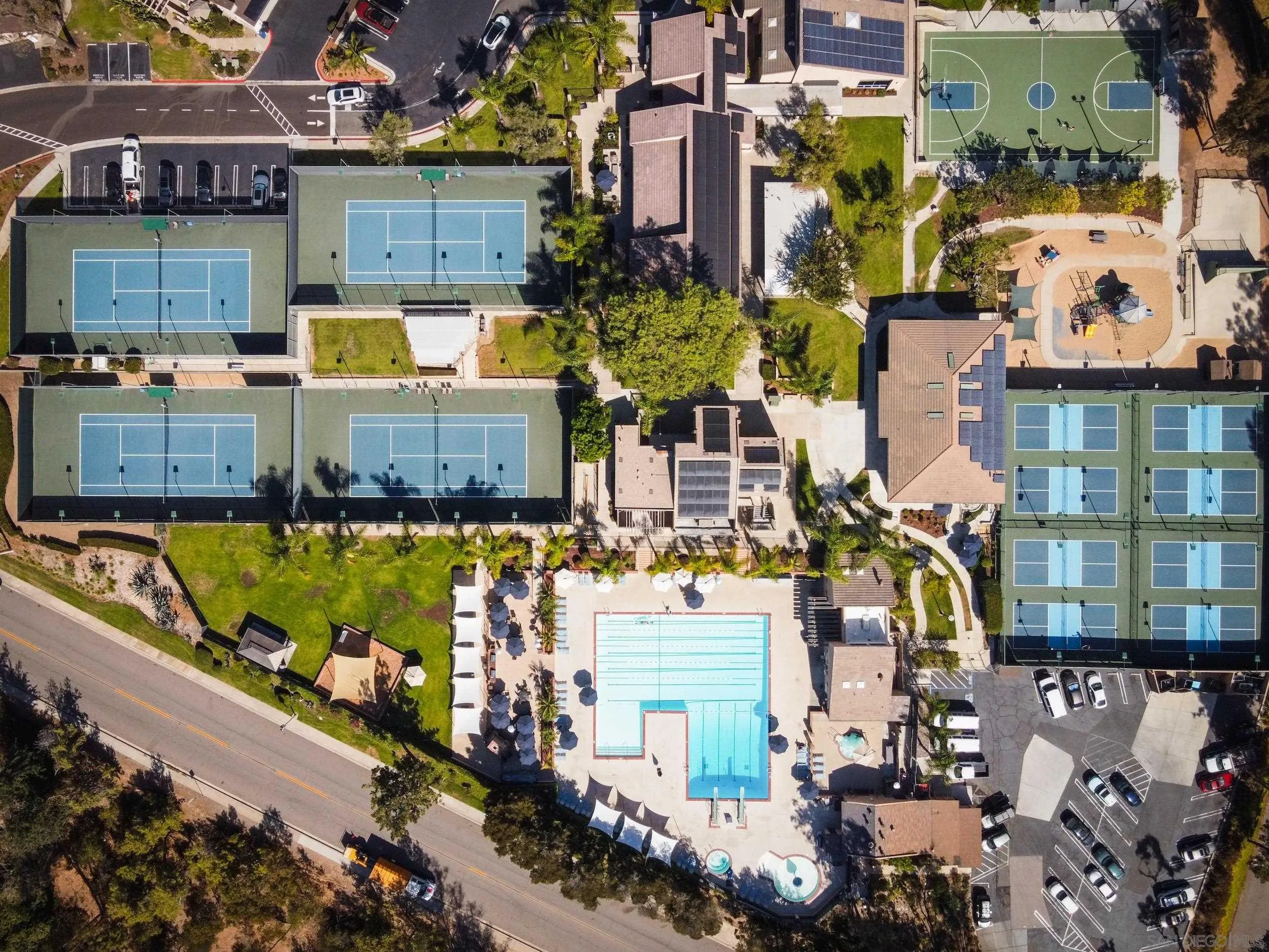 Aerial view of community amenities with tennis courts, a swimming pool, basketball court, and playground.
