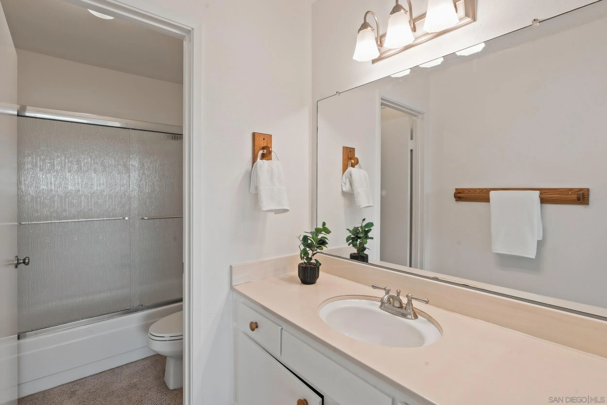 Bathroom with a long vanity and large mirror beside a tub-shower with textured glass doors.