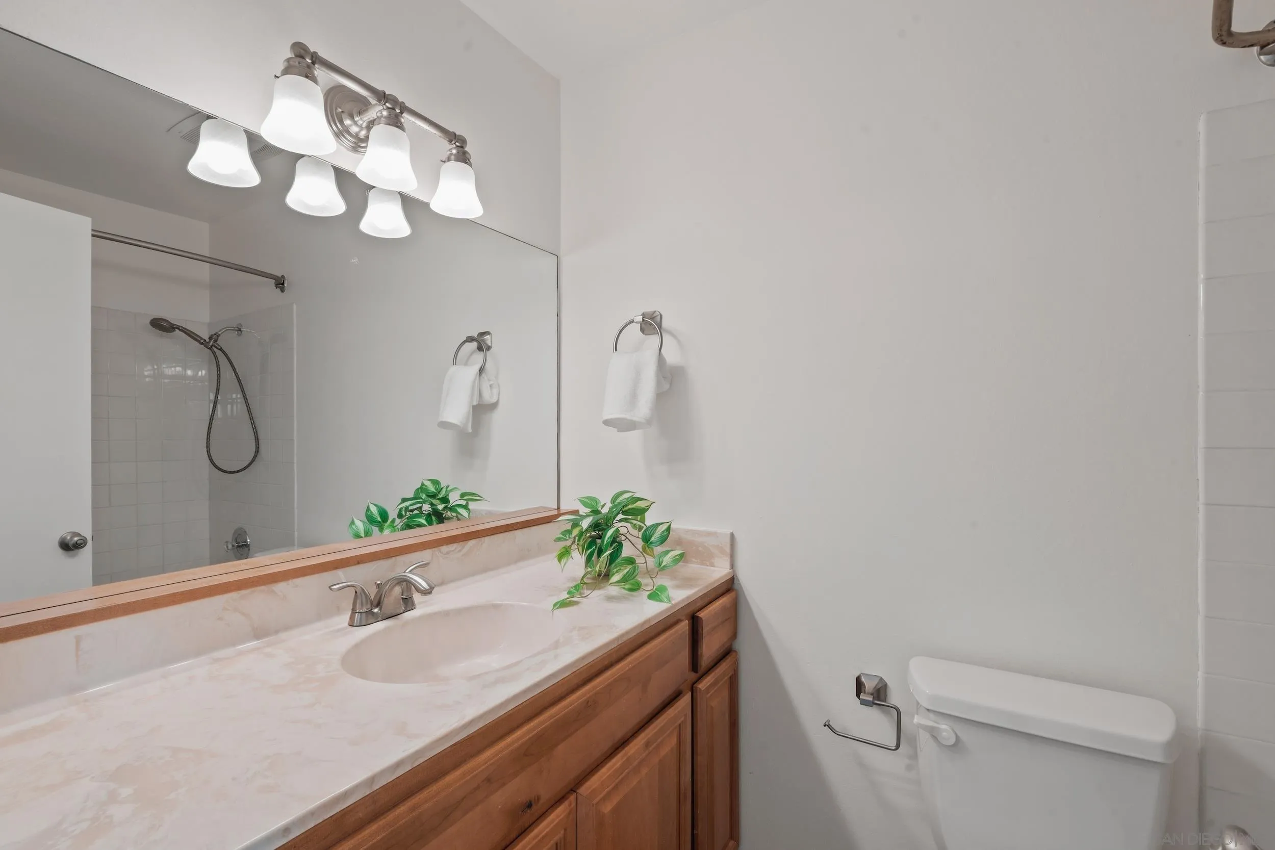 Bathroom with a wood vanity, pale stone countertop, large mirror, and tiled shower.