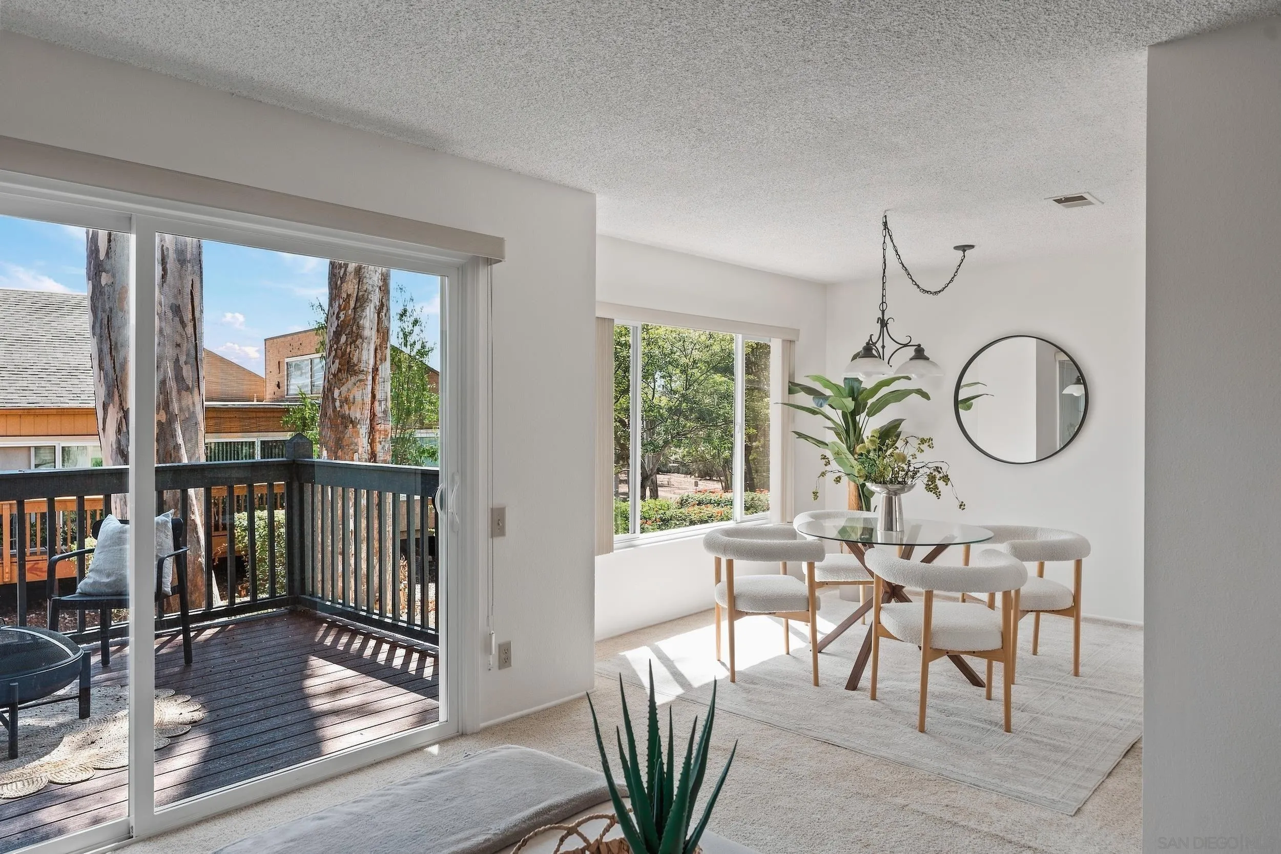 Dining area with a round glass table and sliding doors opening onto a tree-lined balcony.