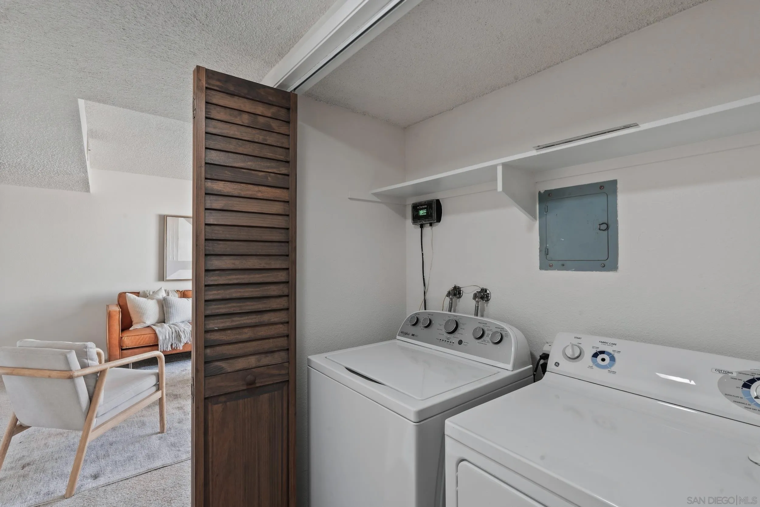 Laundry room with a washer and dryer beside a dark wooden louvered door.
