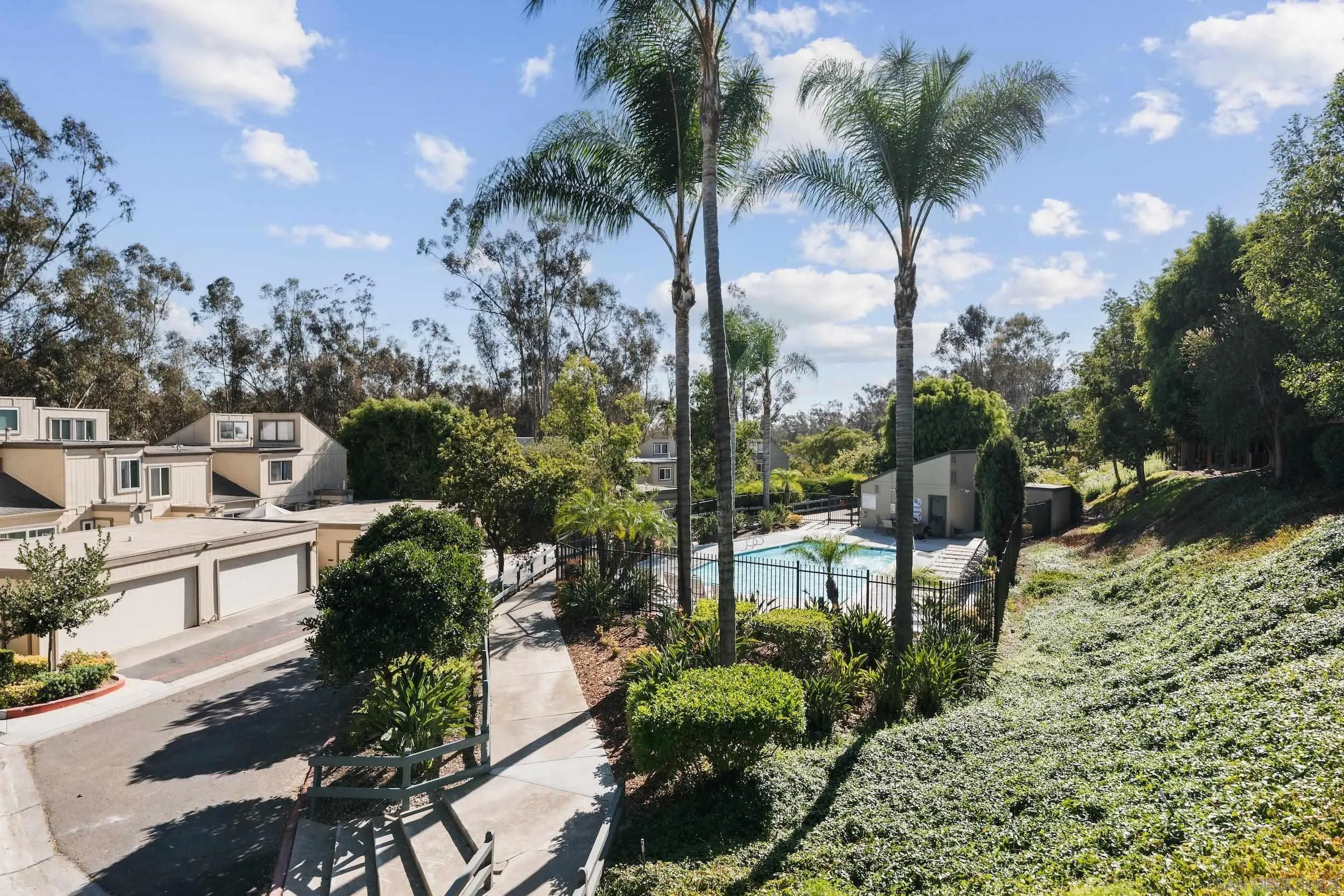 Condominium community pool surrounded by palm trees, garages, and landscaped grounds.