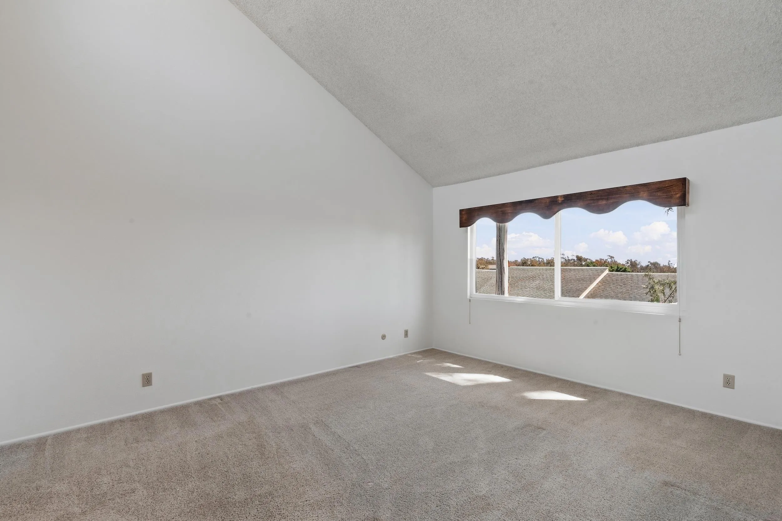 Empty carpeted bedroom with a wide window and dark wood valance.