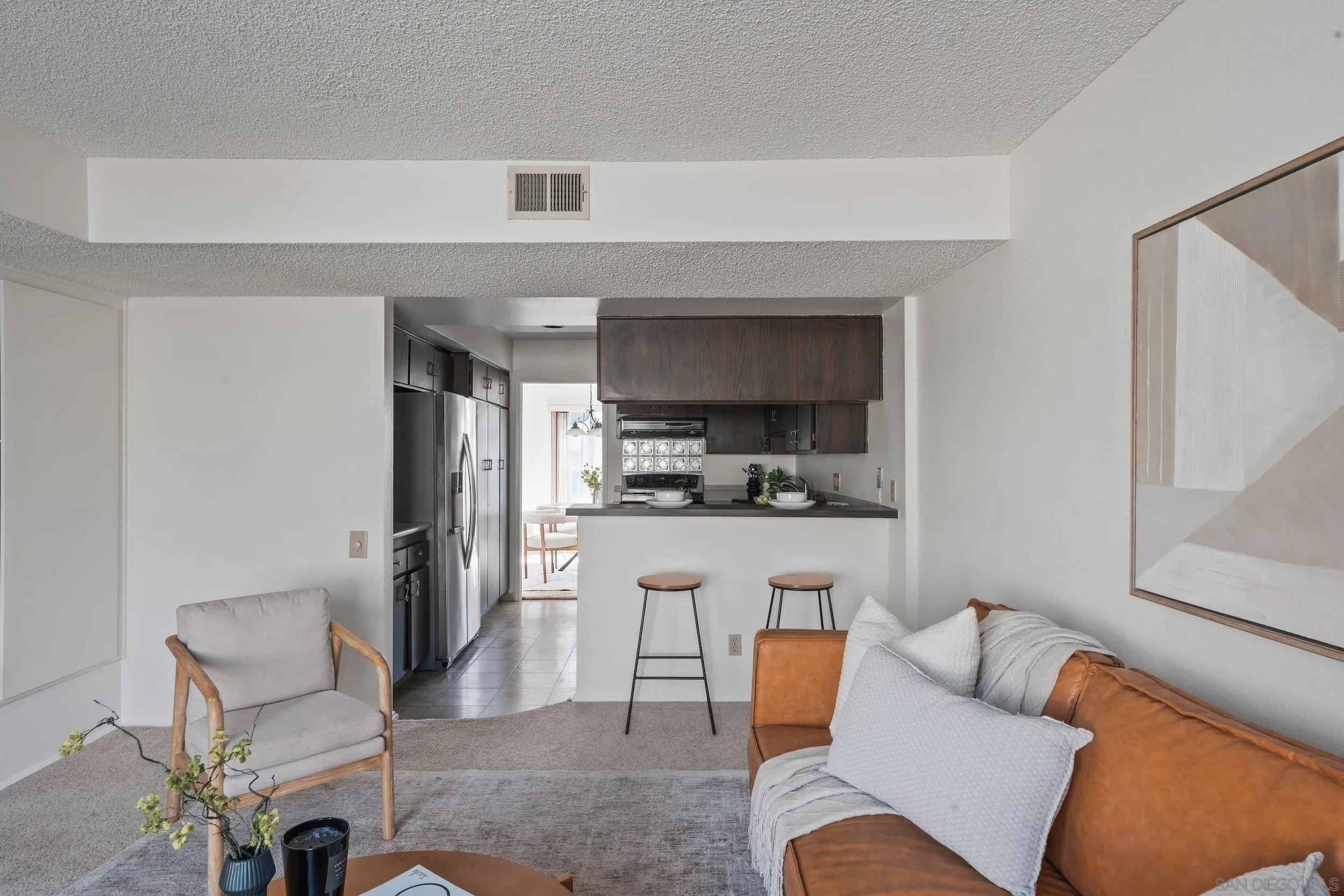 Open-plan living room and kitchen with a caramel leather sofa, breakfast bar, and dark cabinetry.