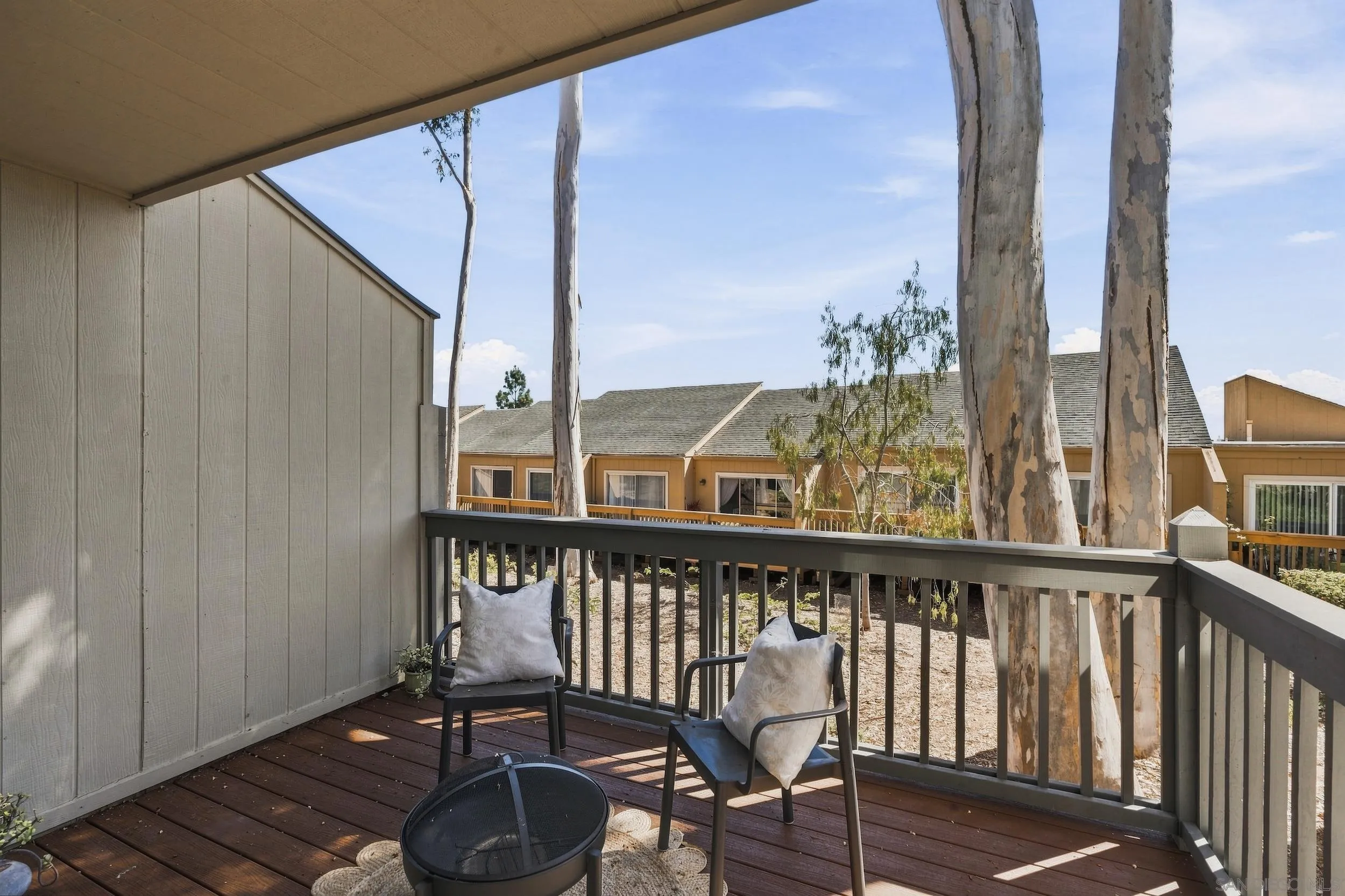 Wooden balcony with two cushioned chairs overlooking tall eucalyptus trees and neighboring homes.