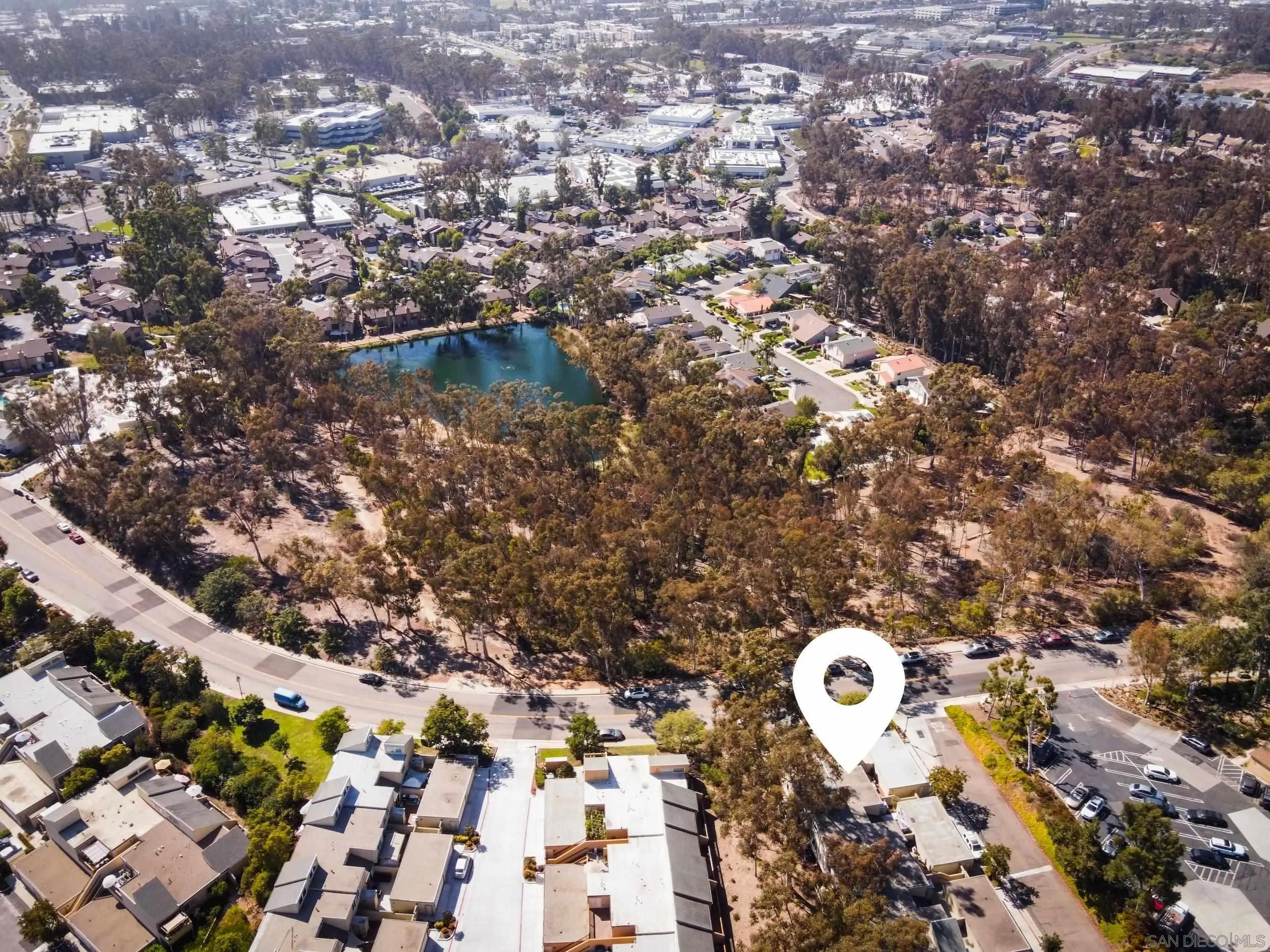Aerial view of a residential neighborhood, with a location marker beside a tree-lined pond.