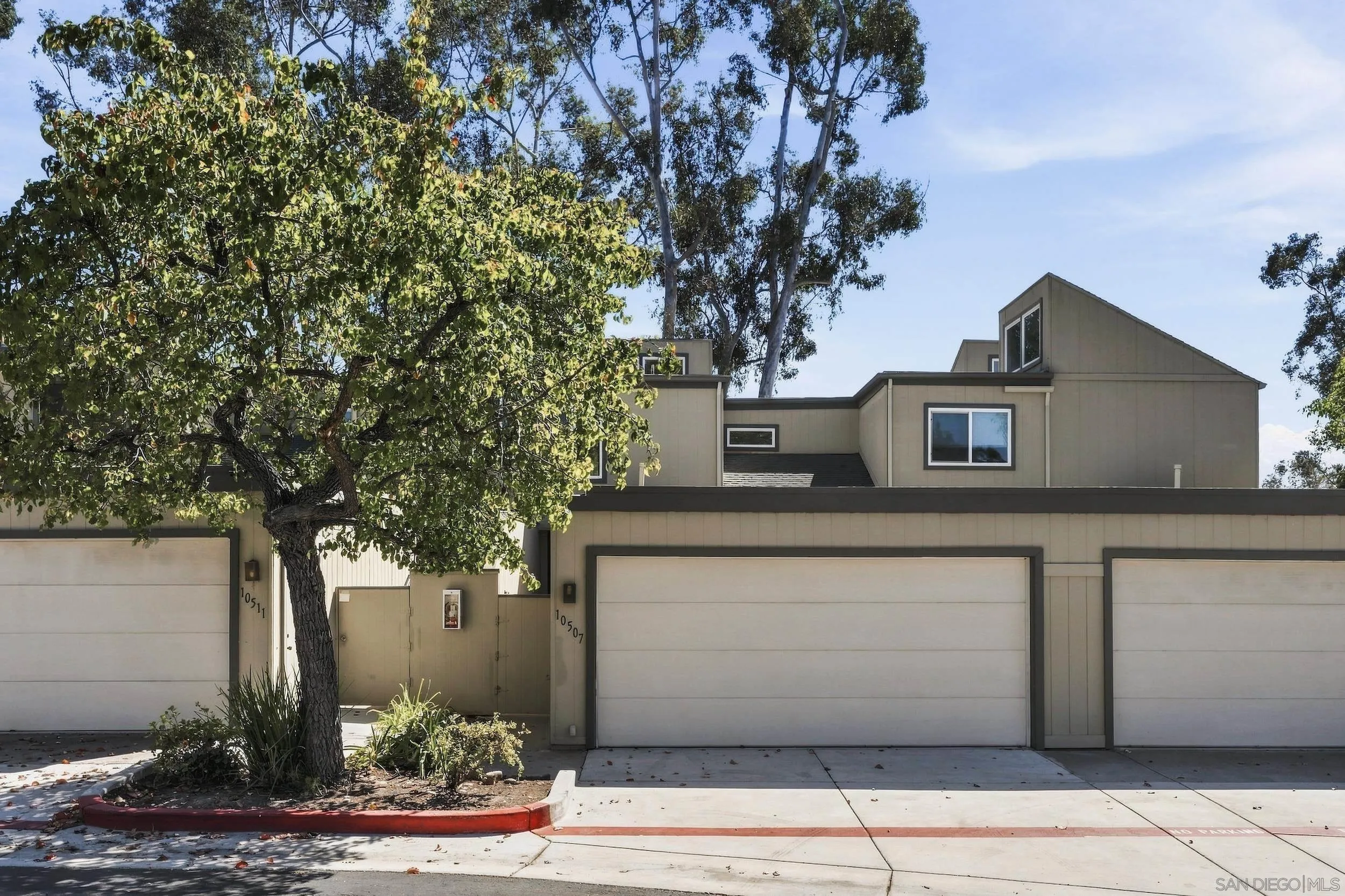 Beige multi-level home with attached garages, partly screened by a large leafy tree.