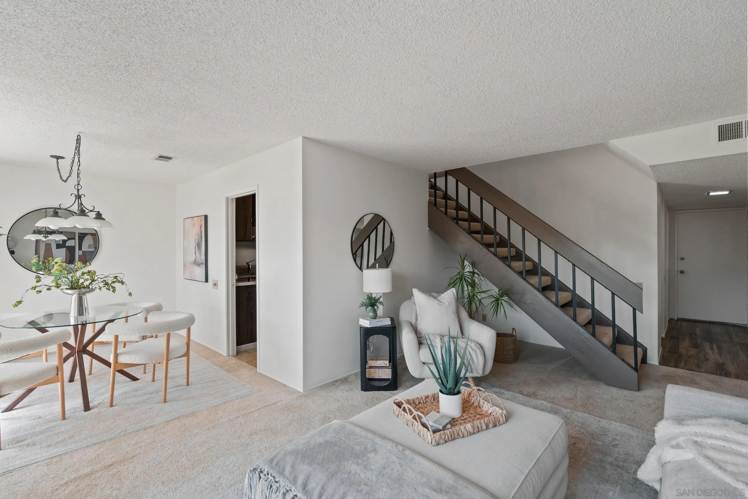 Open-plan living and dining area with white seating, a glass table, and a carpeted staircase.