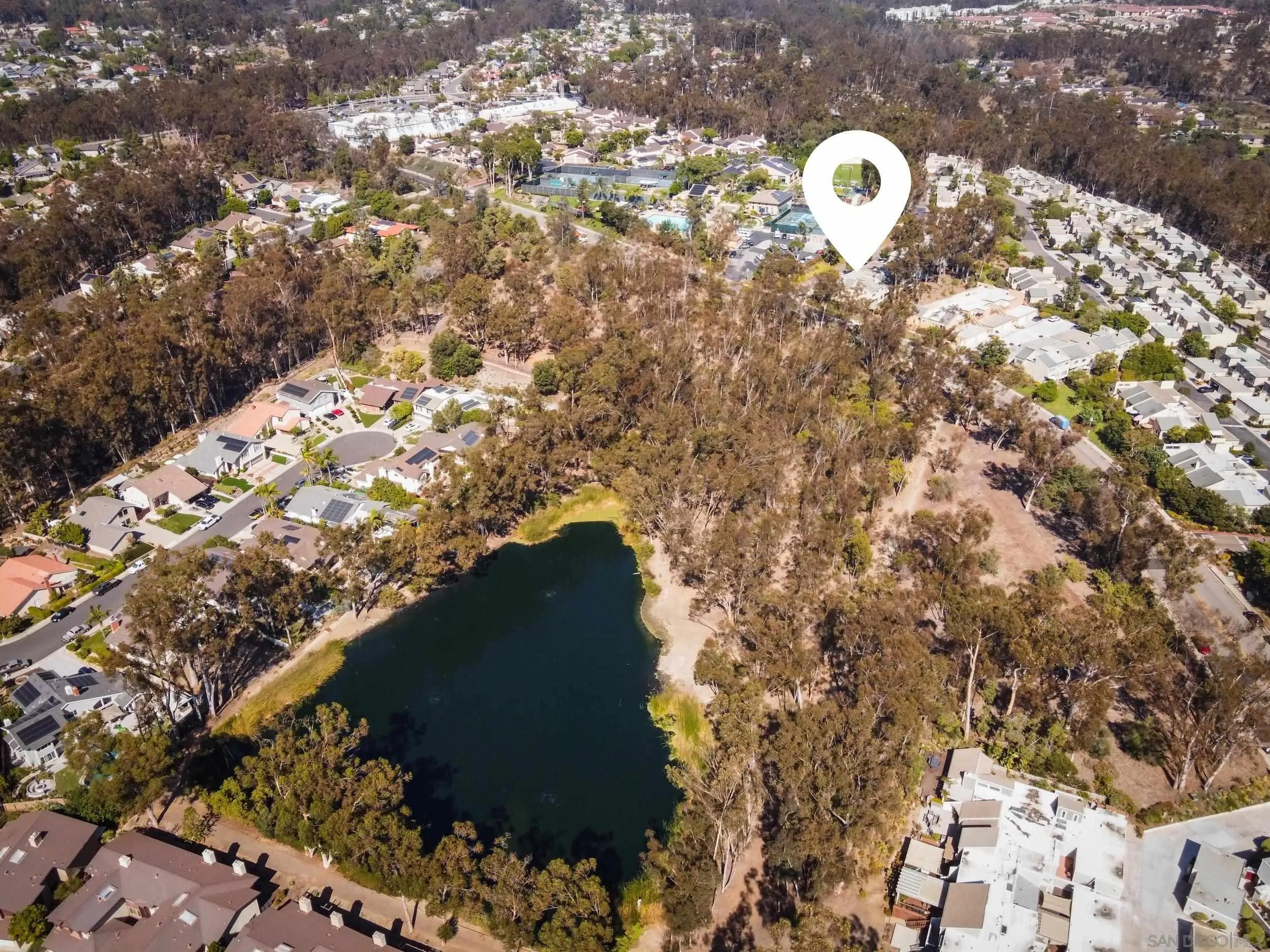 Aerial view of the property location, marked by a white pin beside a tree-lined lake and neighborhood homes.