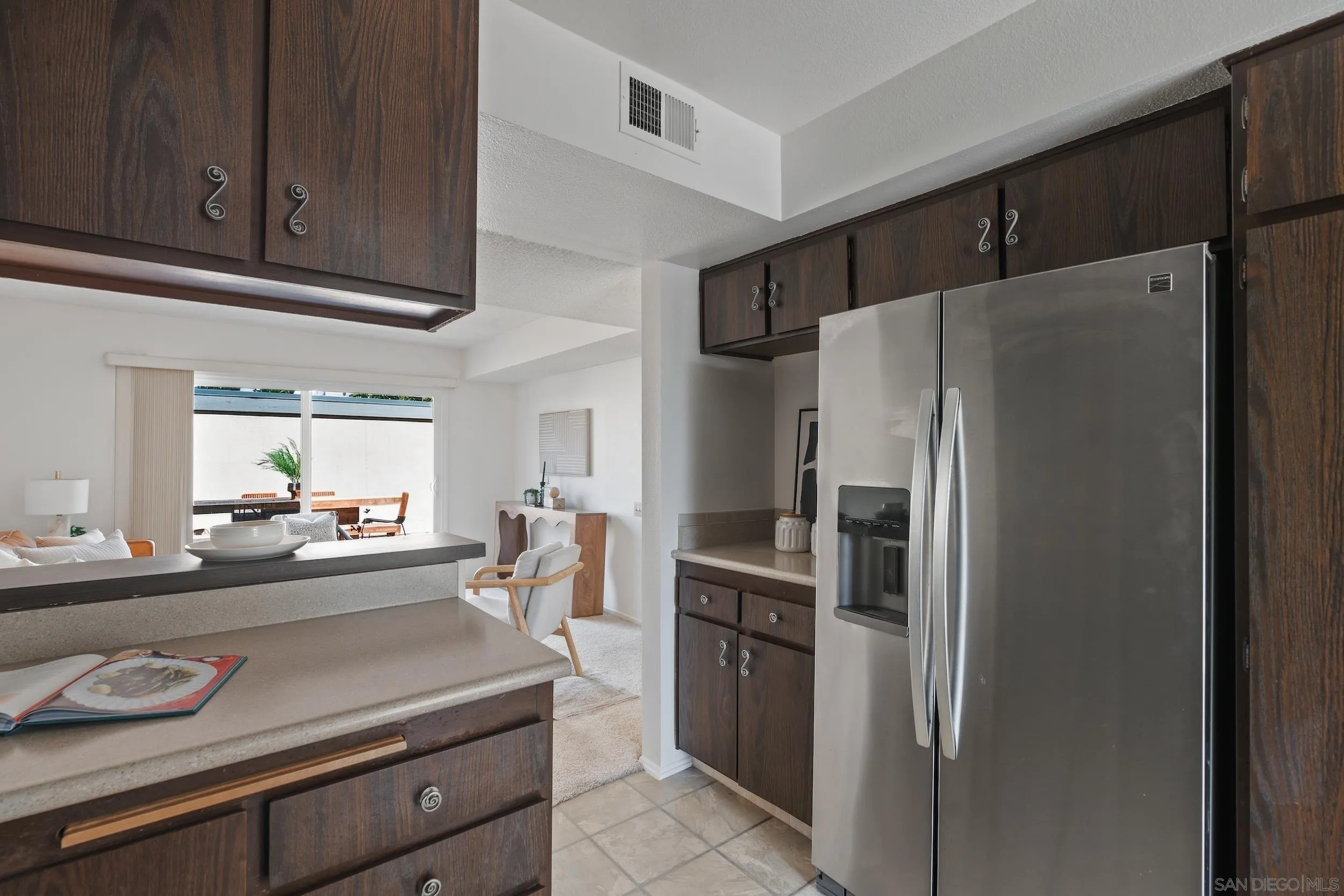 Kitchen with dark wood cabinets, light counters, and a stainless-steel refrigerator.