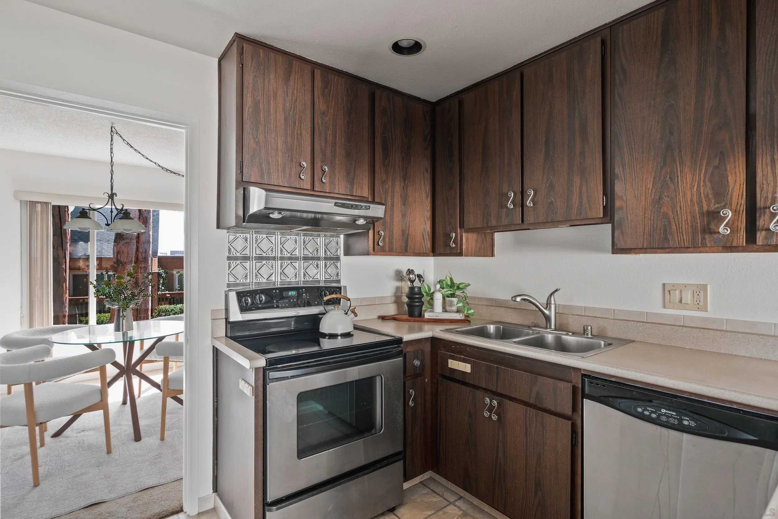 Kitchen with dark wood cabinets, stainless appliances, patterned tile backsplash, and an adjoining glass-table dining nook.