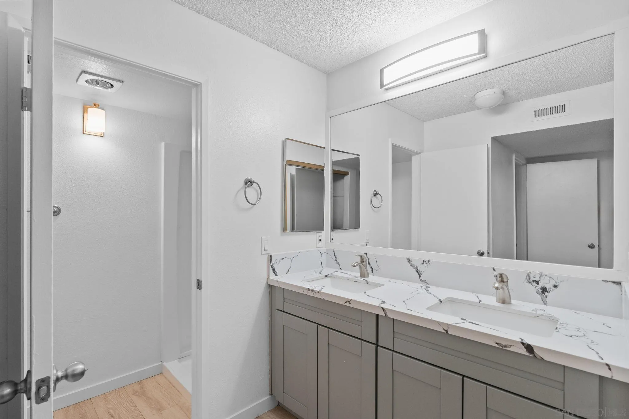 Bathroom with a gray double vanity, two sinks, marble-pattern counters, and a wall-length mirror.