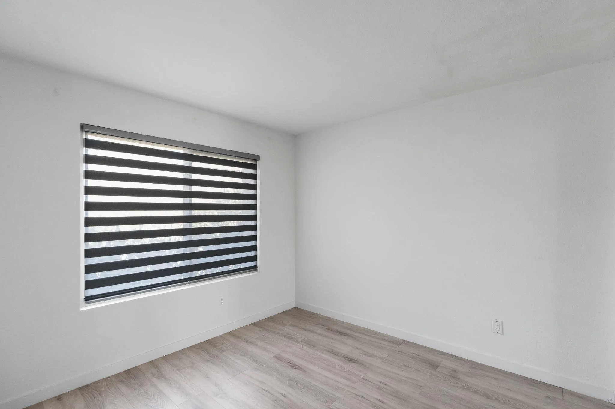 Empty room with light wood-look flooring and a large window with striped blinds.