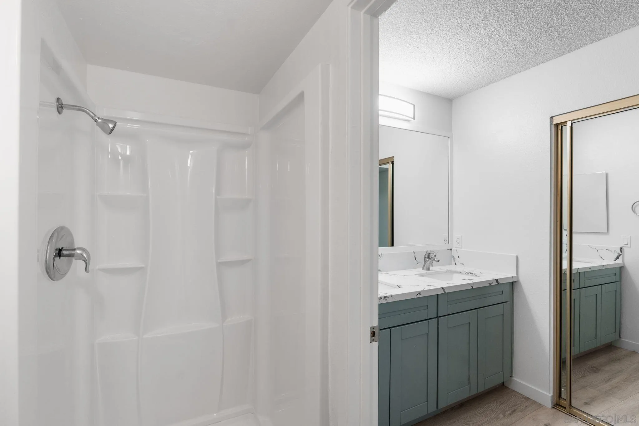 Bathroom with a white shower enclosure and gray-green vanity topped by a veined countertop.