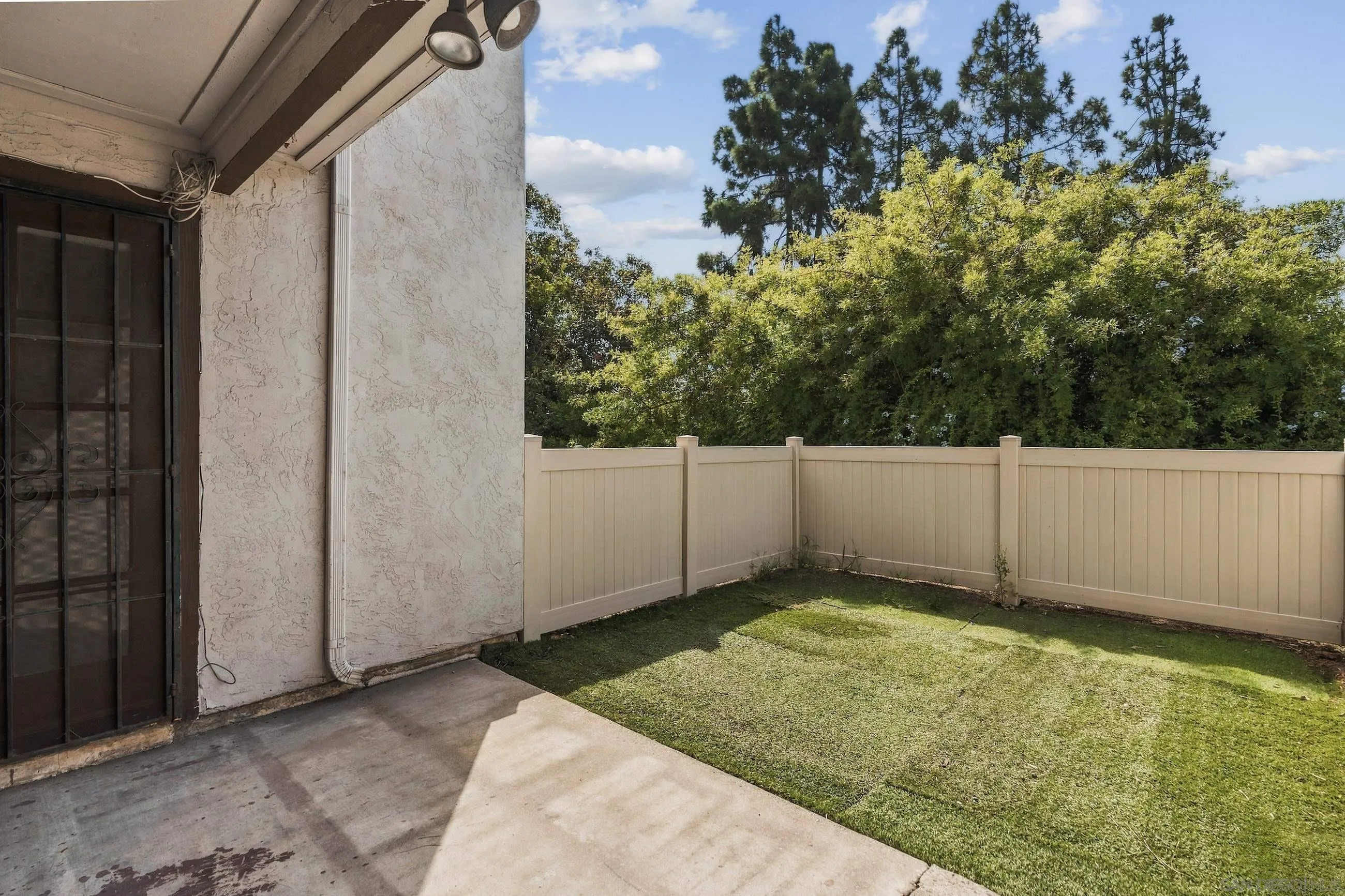 Fenced backyard with a lawn and covered patio beside a stucco home.