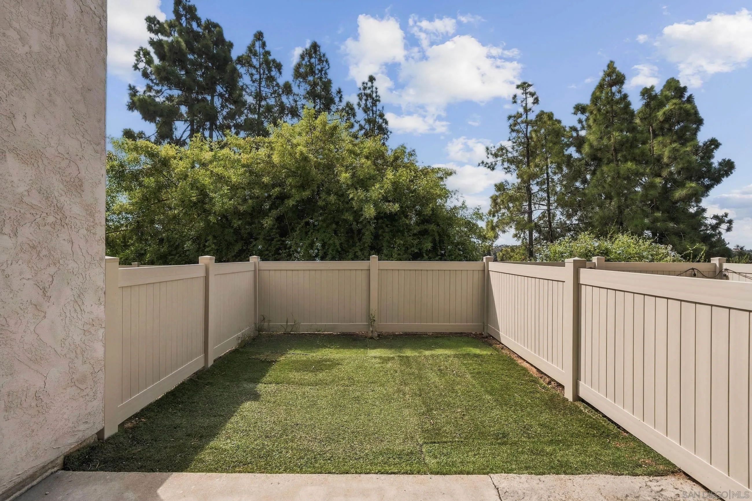 Fenced backyard with a grass lawn, beige privacy fence, and mature trees.