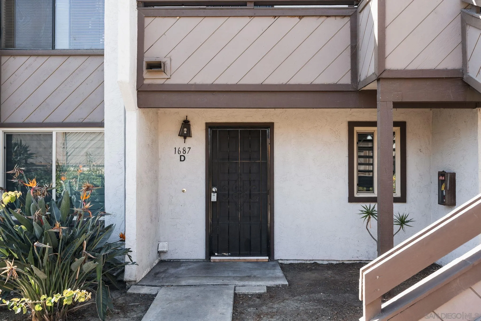 Unit D entrance with a black security door, covered porch, and tropical landscaping.