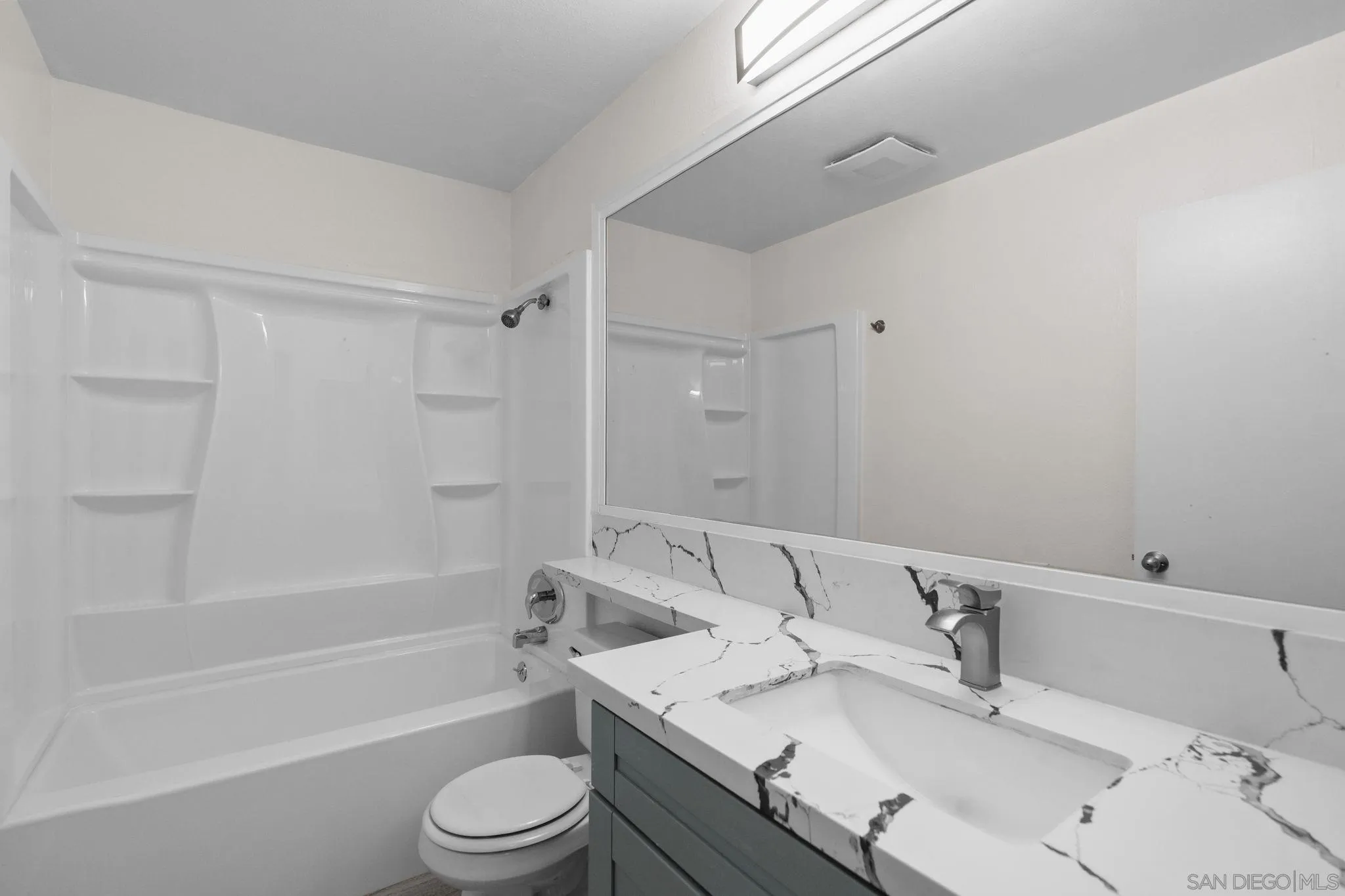 Bathroom with a tub and shower beside a gray vanity with a veined white countertop.
