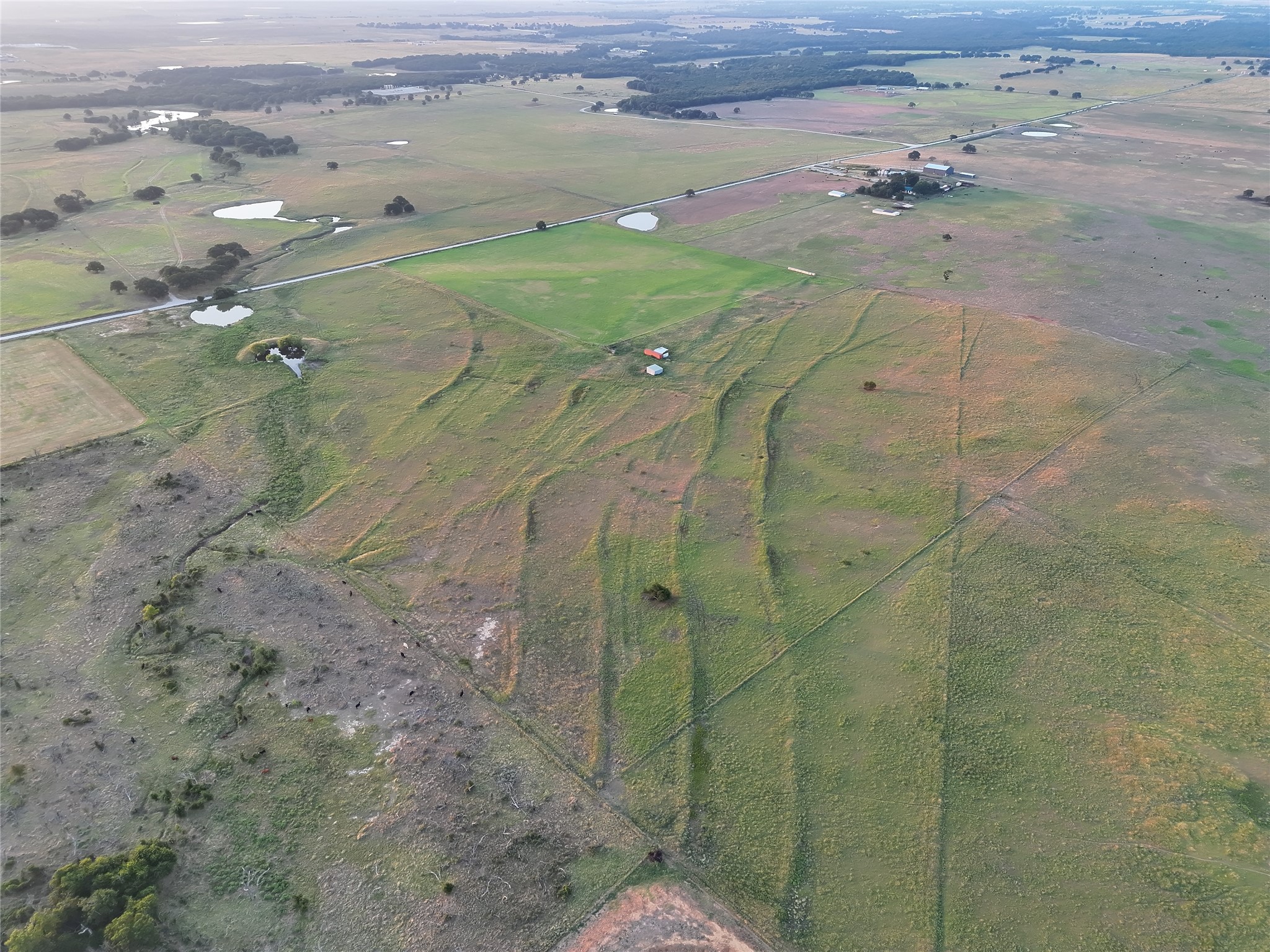 Aerial view of rural acreage with patchwork fields, several ponds, and small outbuildings.