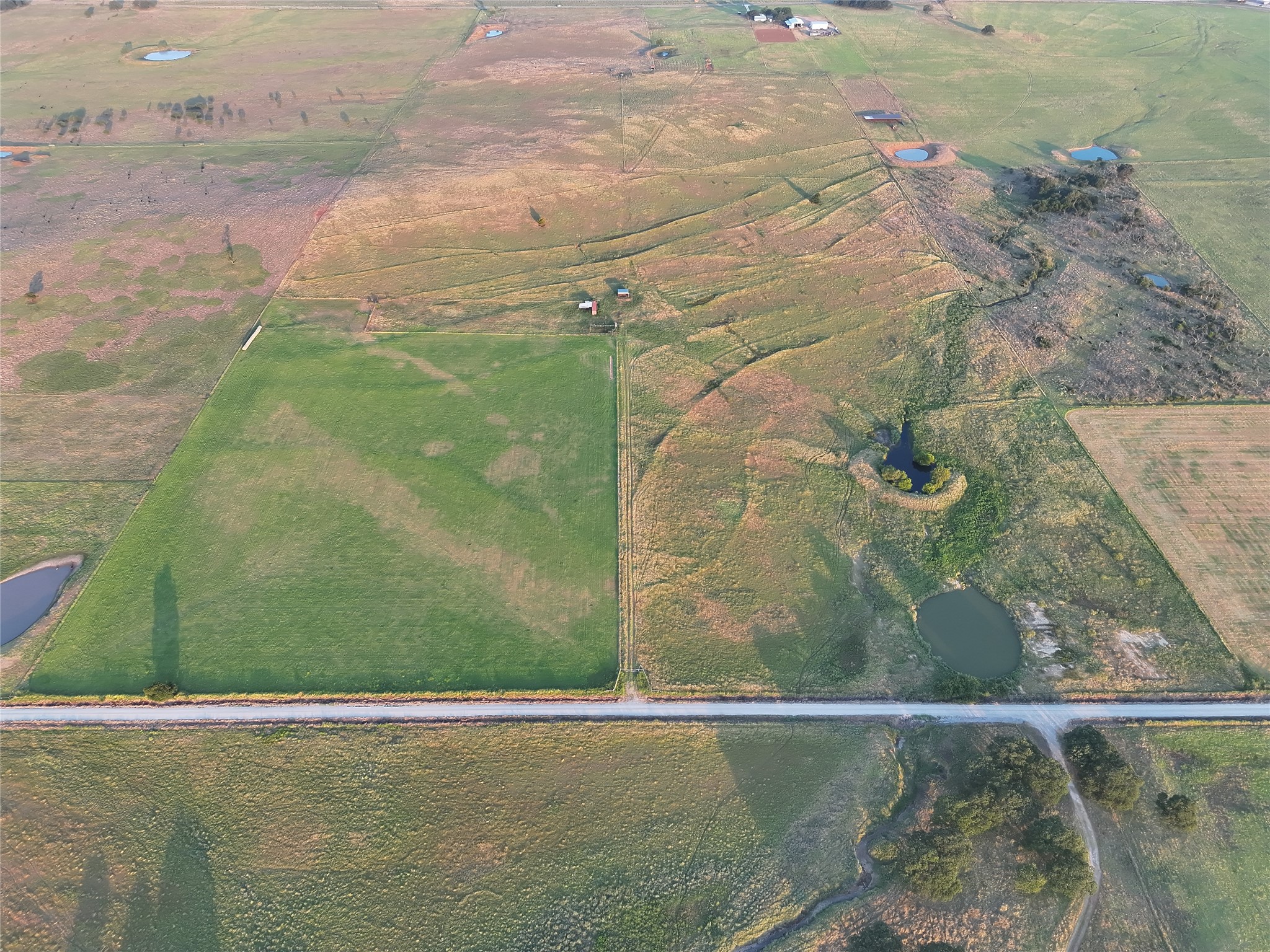Aerial pastureland with ponds, a creek, and a road along its edge.