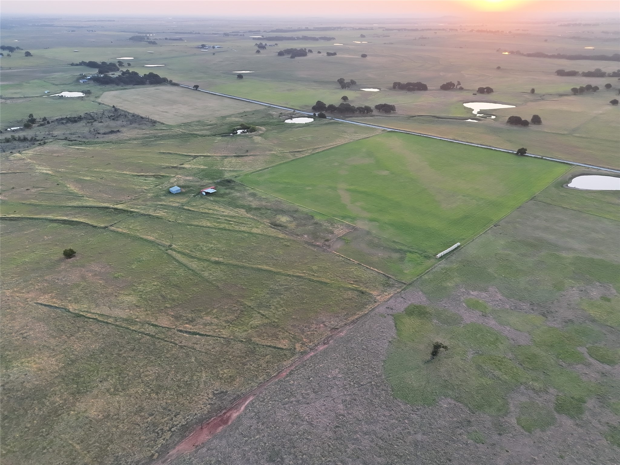 Aerial view of rural fields and ponds, with a diagonal road and two small outbuildings.
