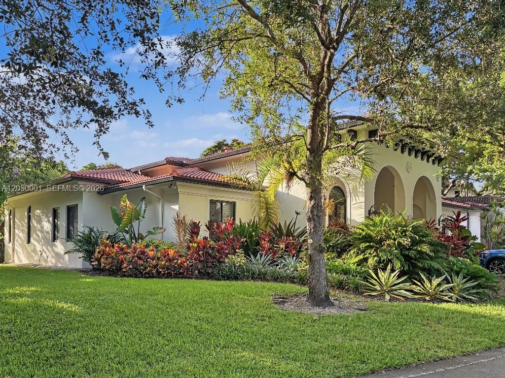 Cream-colored home with red tile roof, arched entrance, tropical landscaping, and broad lawn.