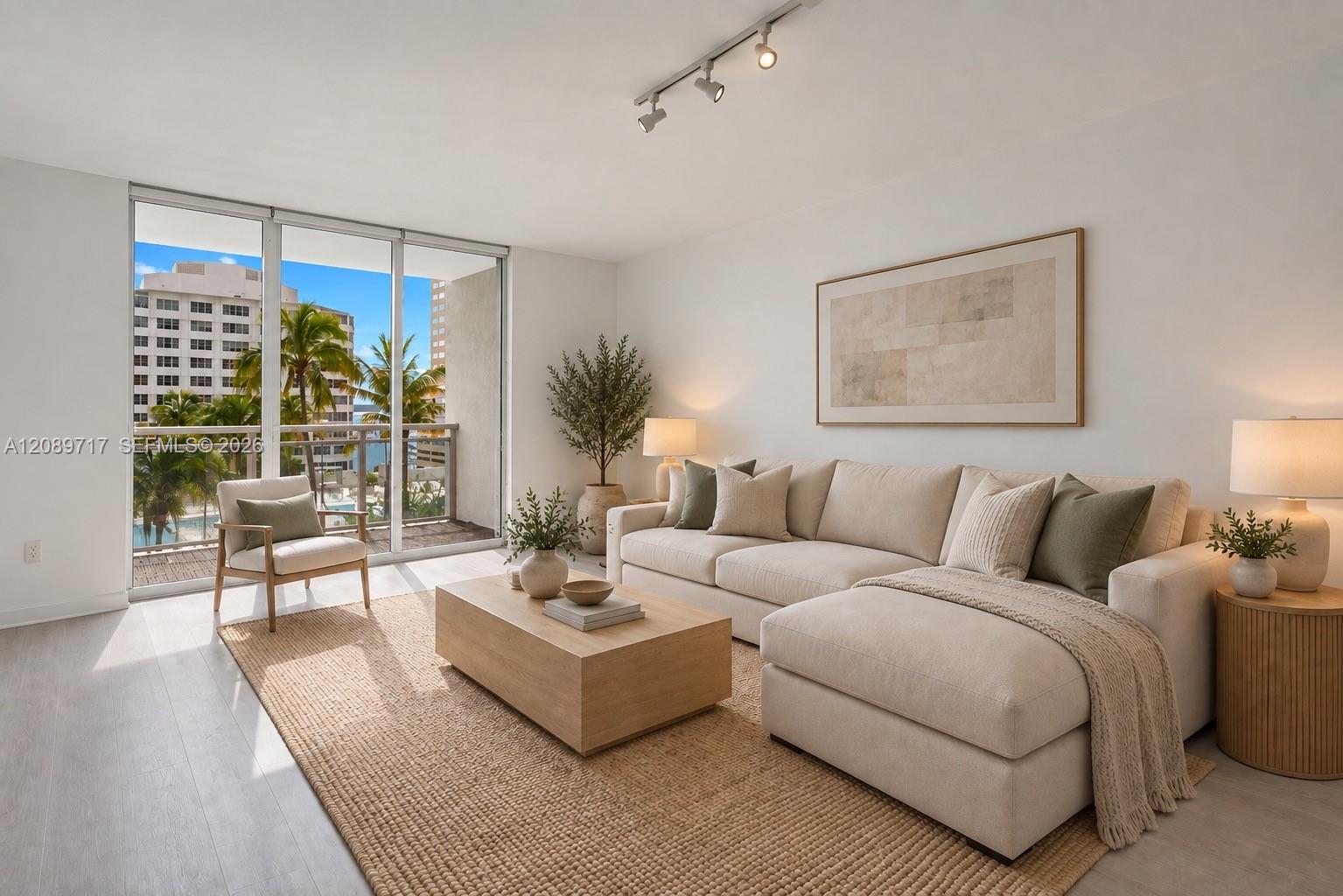 Staged living room with a cream sectional and balcony windows overlooking palm trees and city buildings.
