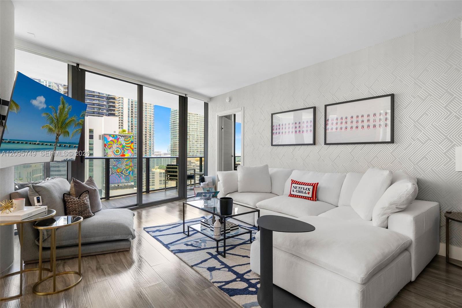 Modern condo living room with a white sectional, patterned rug, and floor-to-ceiling windows overlooking downtown buildings.