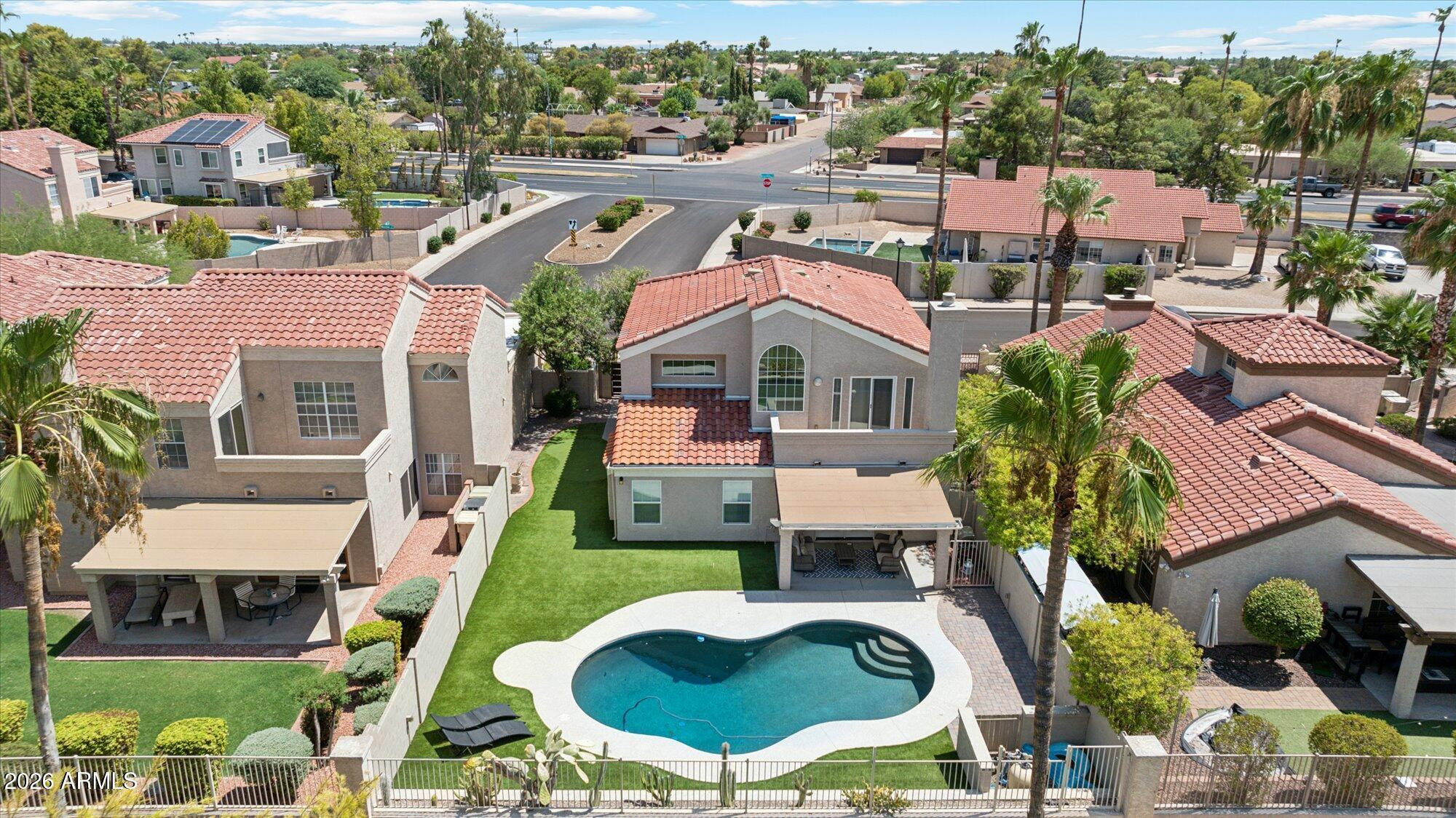Aerial view of a home with a curving swimming pool, lawn, and covered patio.
