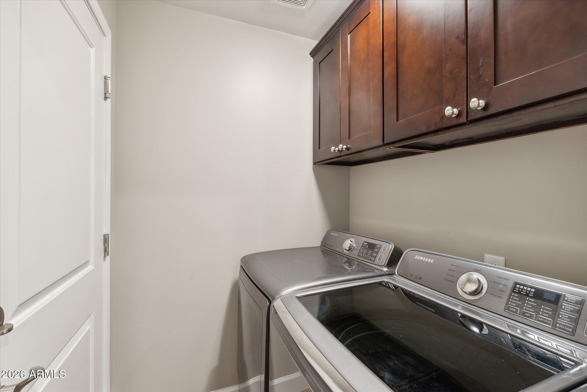 Laundry room with front-loading washer and dryer beneath dark wood cabinets.