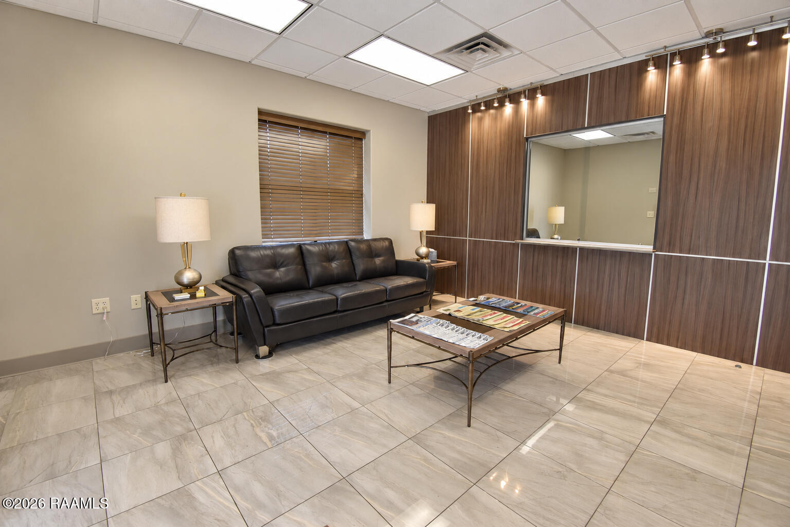 Waiting area with a black leather sofa, magazine tables, and a large mirror on wood-paneled walls.