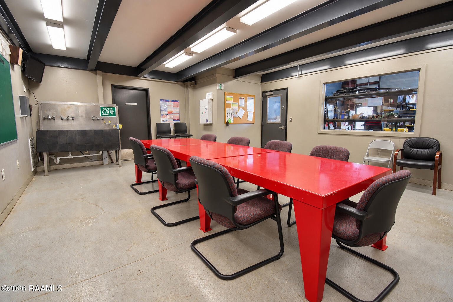 Meeting room with a bright red conference table, upholstered chairs, and a utility sink.