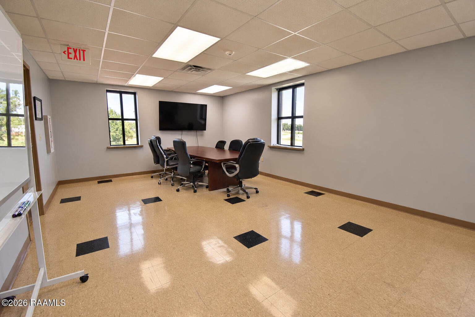 Office conference room with a wooden meeting table, black chairs, and wall-mounted television.