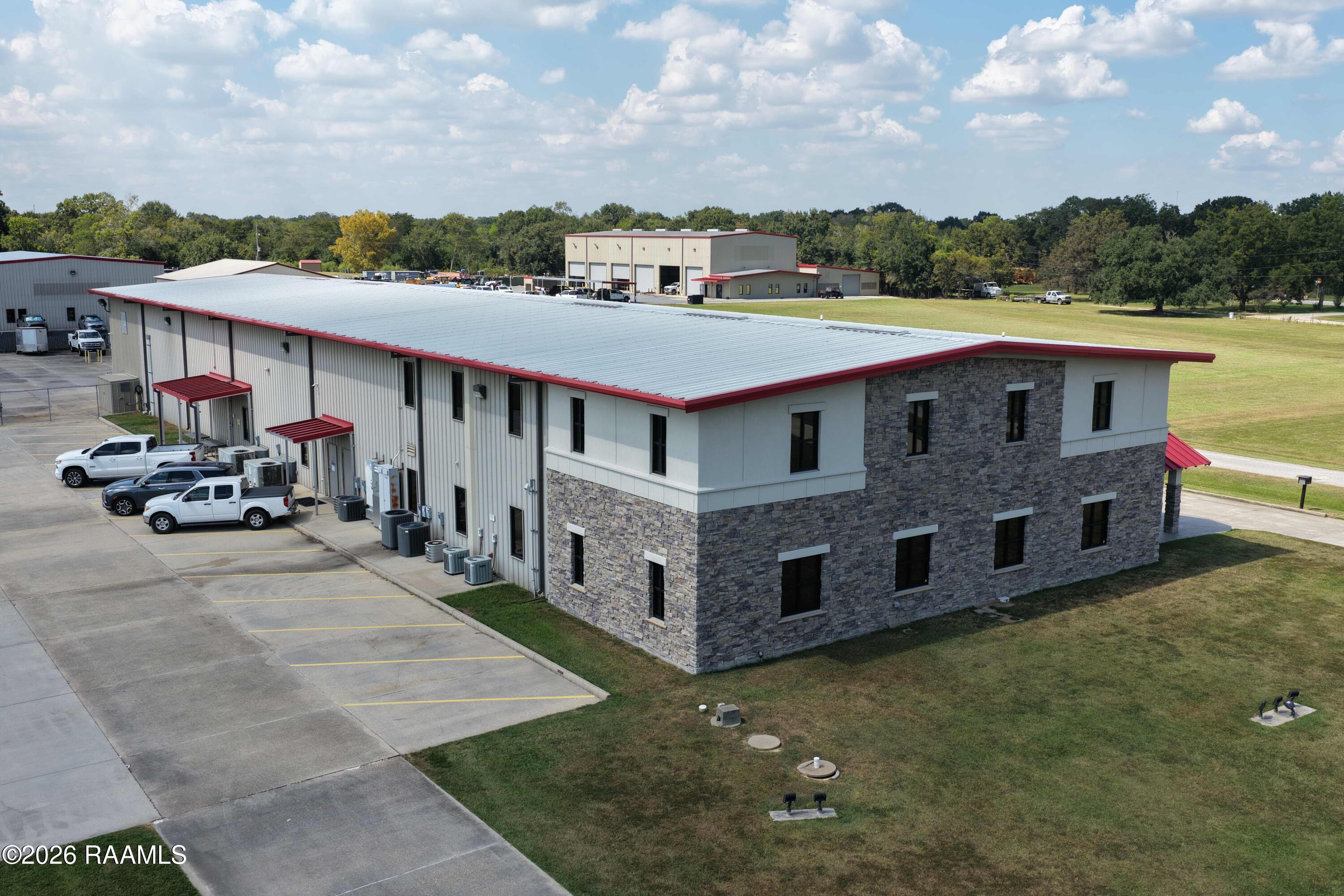 Commercial building with stone and metal siding, red roof trim, and a large parking area.