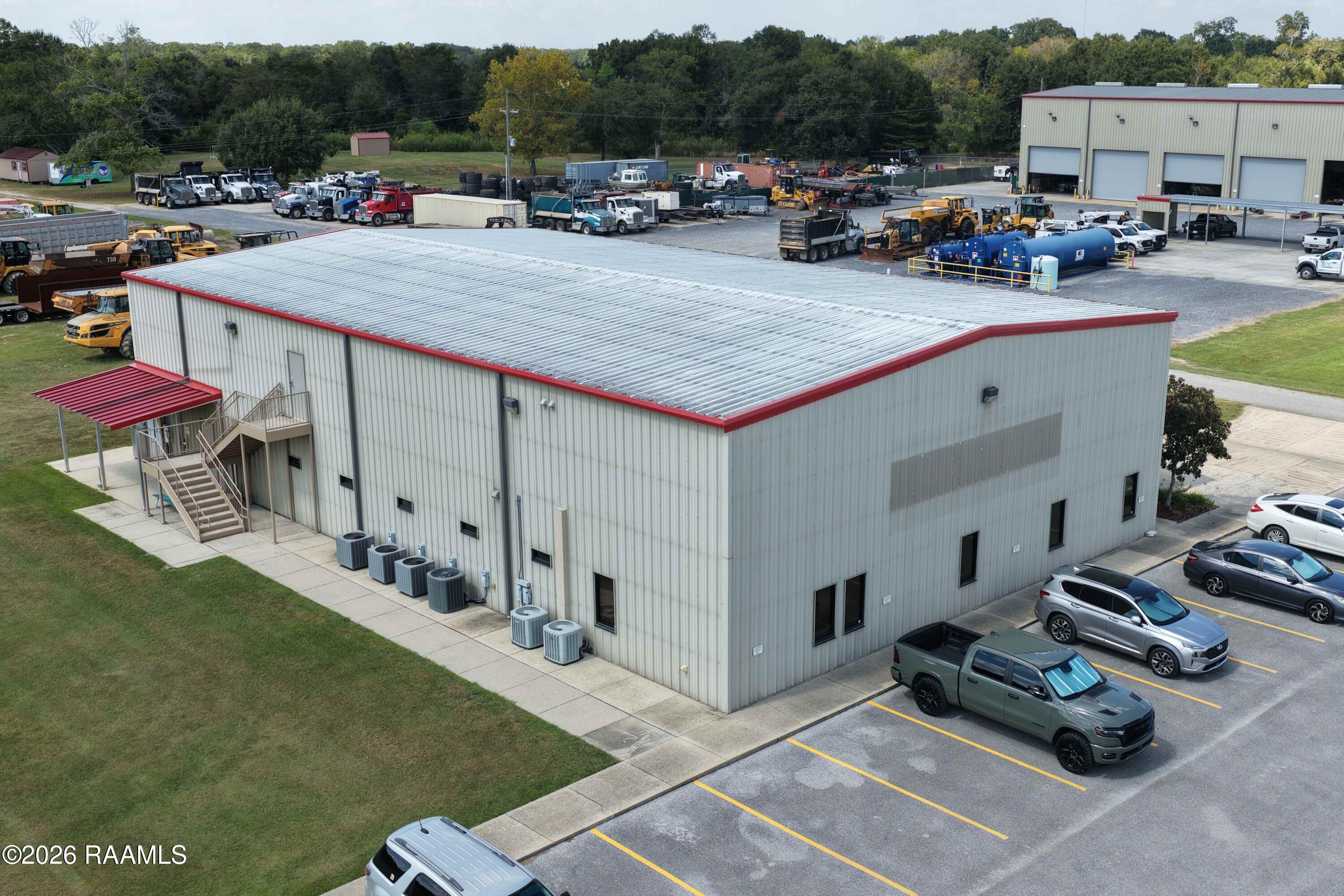 Aerial view of a metal commercial warehouse with red roof trim, parking lot, and work trucks.