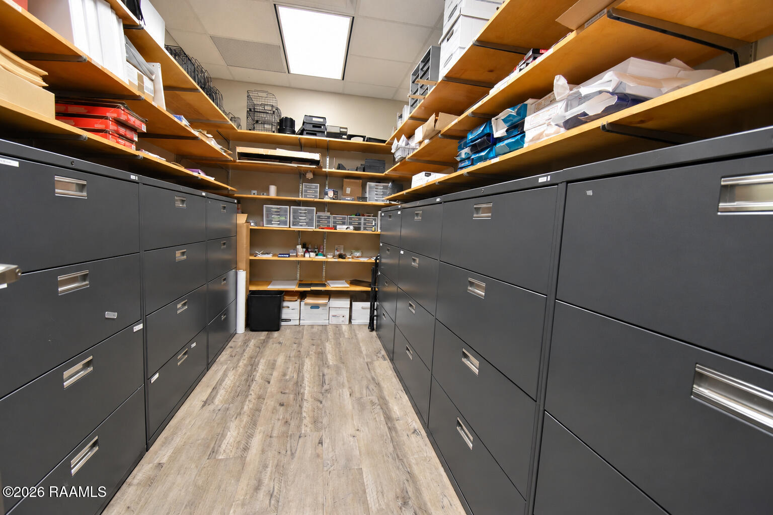 Commercial storage room lined with filing cabinets and stocked wooden shelves.