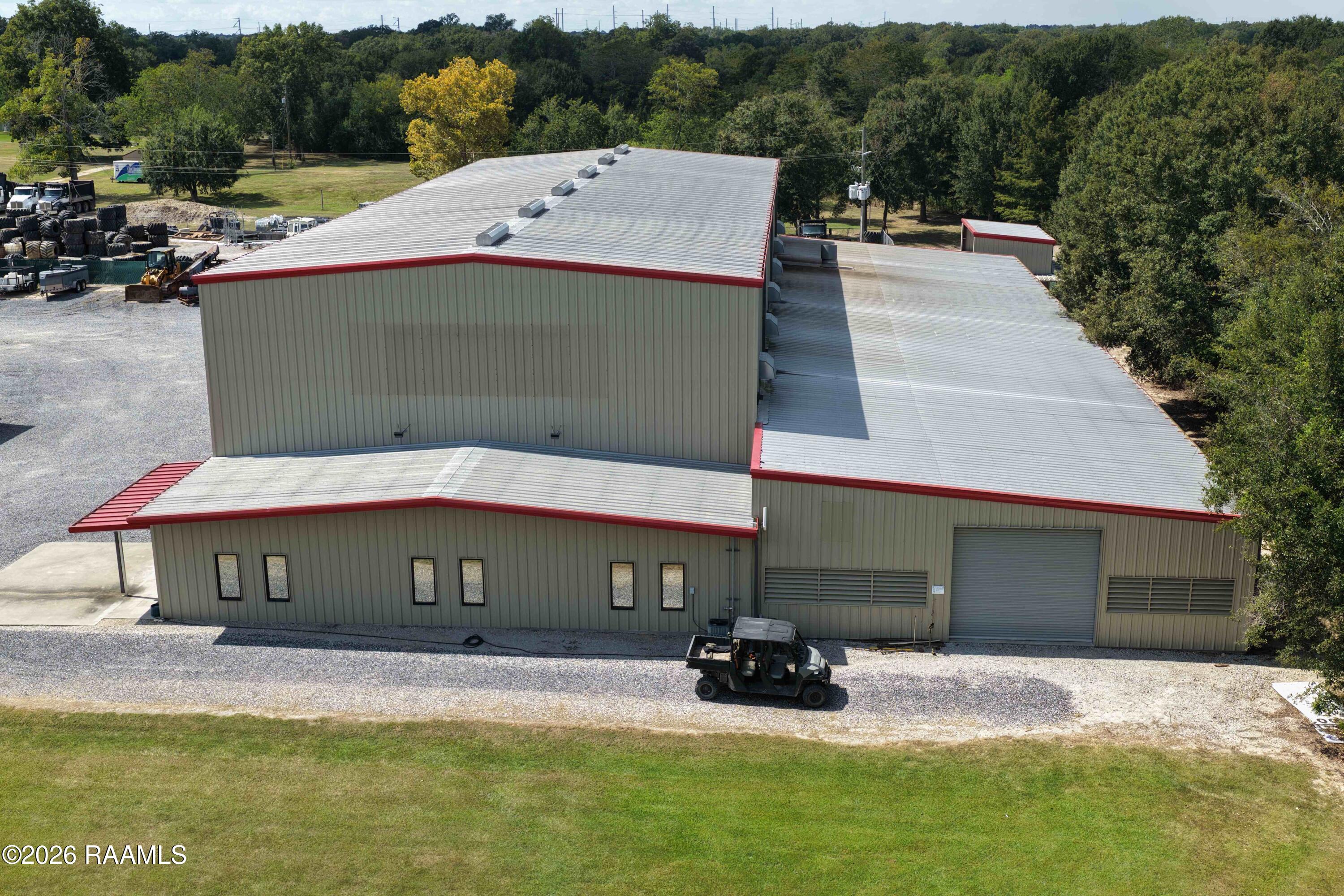 Commercial warehouse with red roof trim, a roll-up door, and a gravel lot, viewed from above.