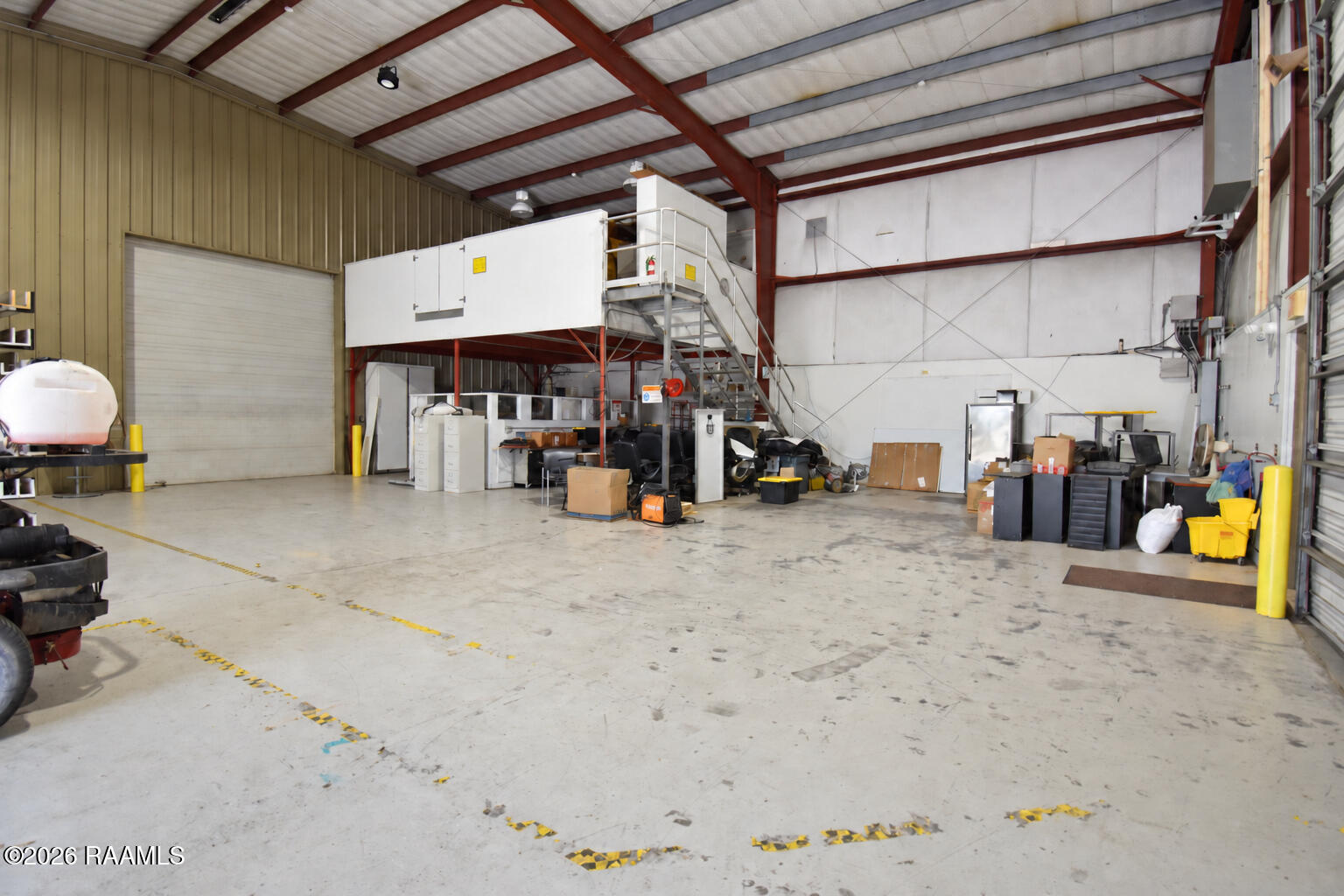 Industrial warehouse interior with a concrete floor, roll-up door, and elevated mezzanine.