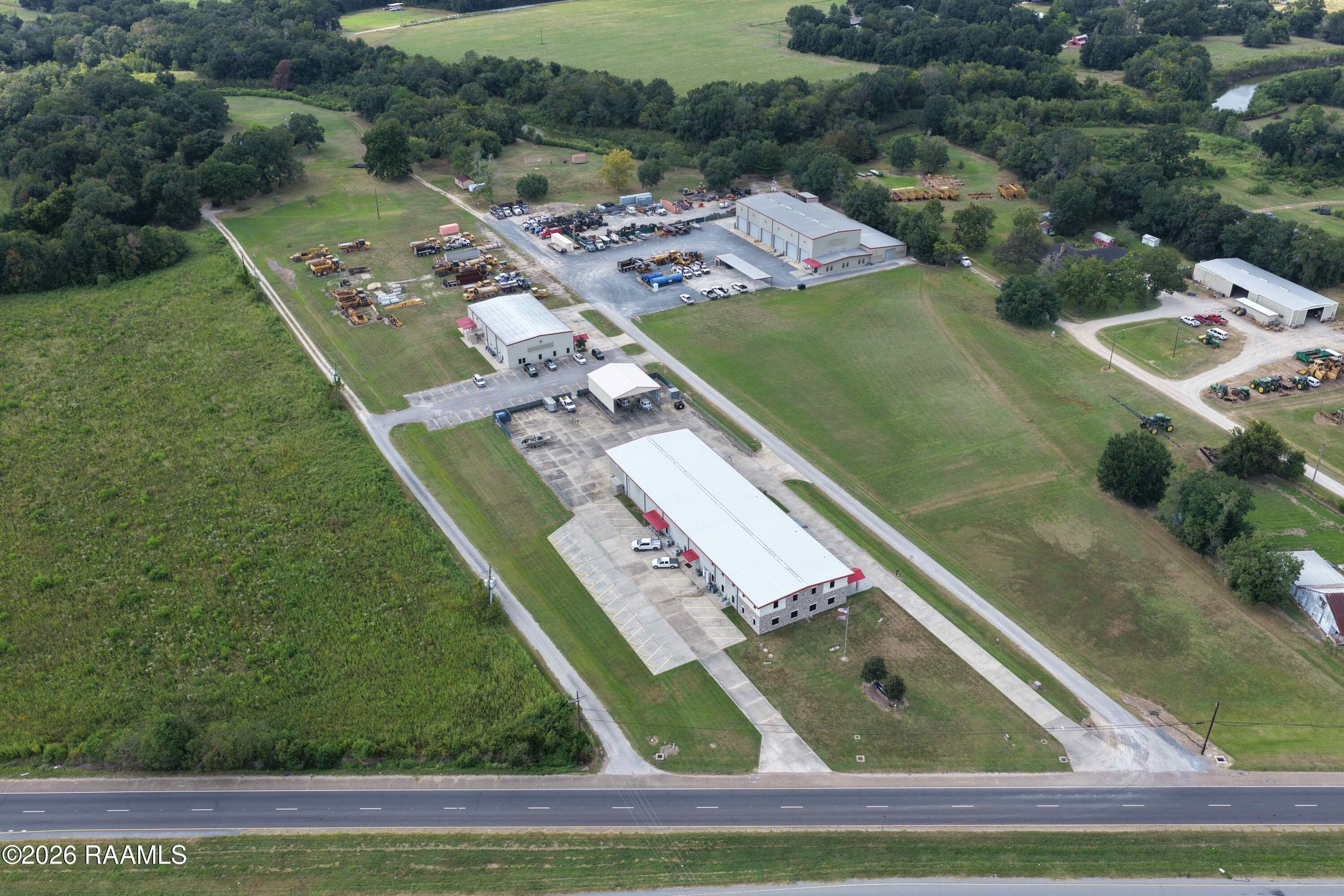 Aerial view of a highway-front commercial property with warehouses and heavy equipment yards.