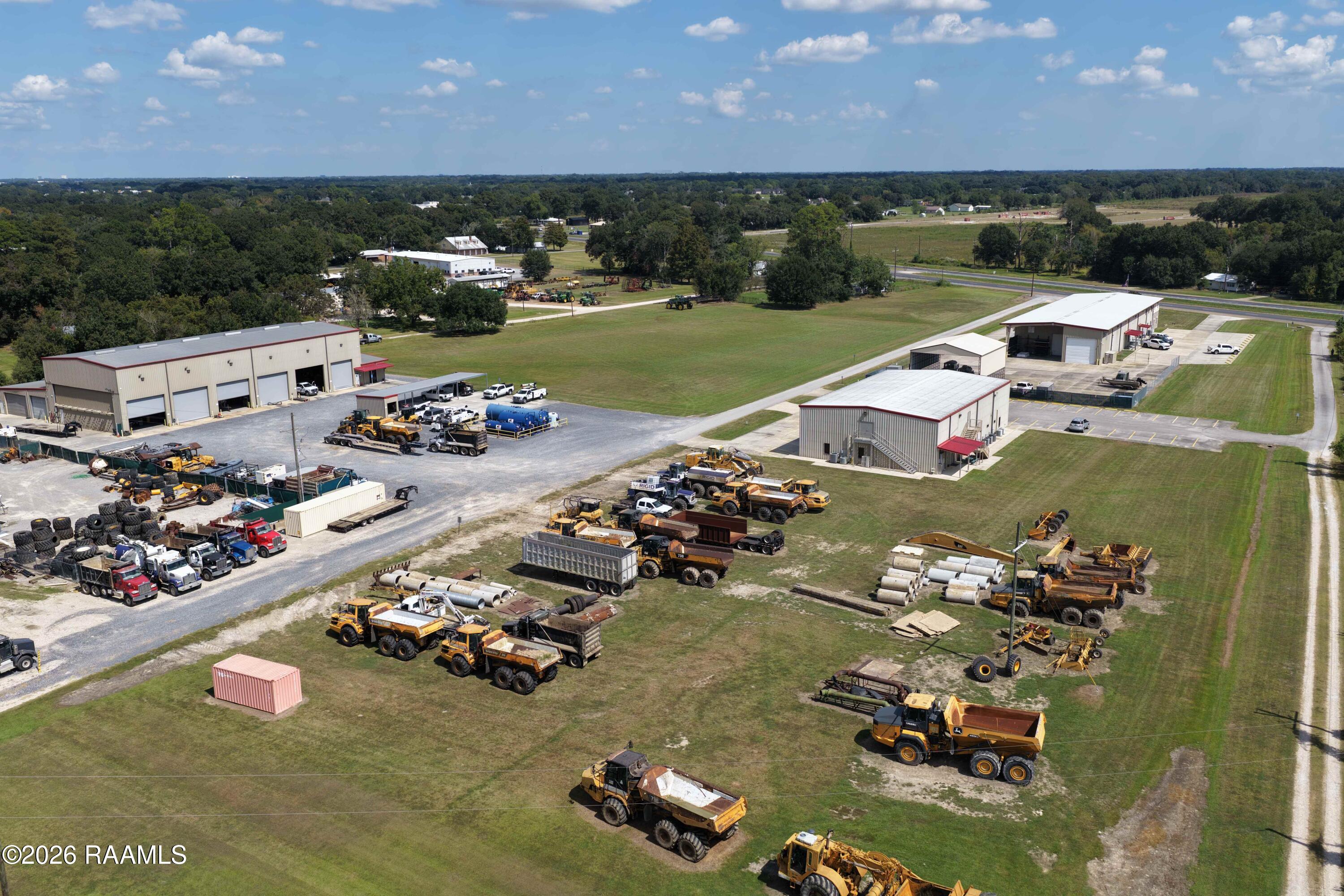 Aerial view of an equipment yard with service buildings, parked construction vehicles, and broad grassy grounds.