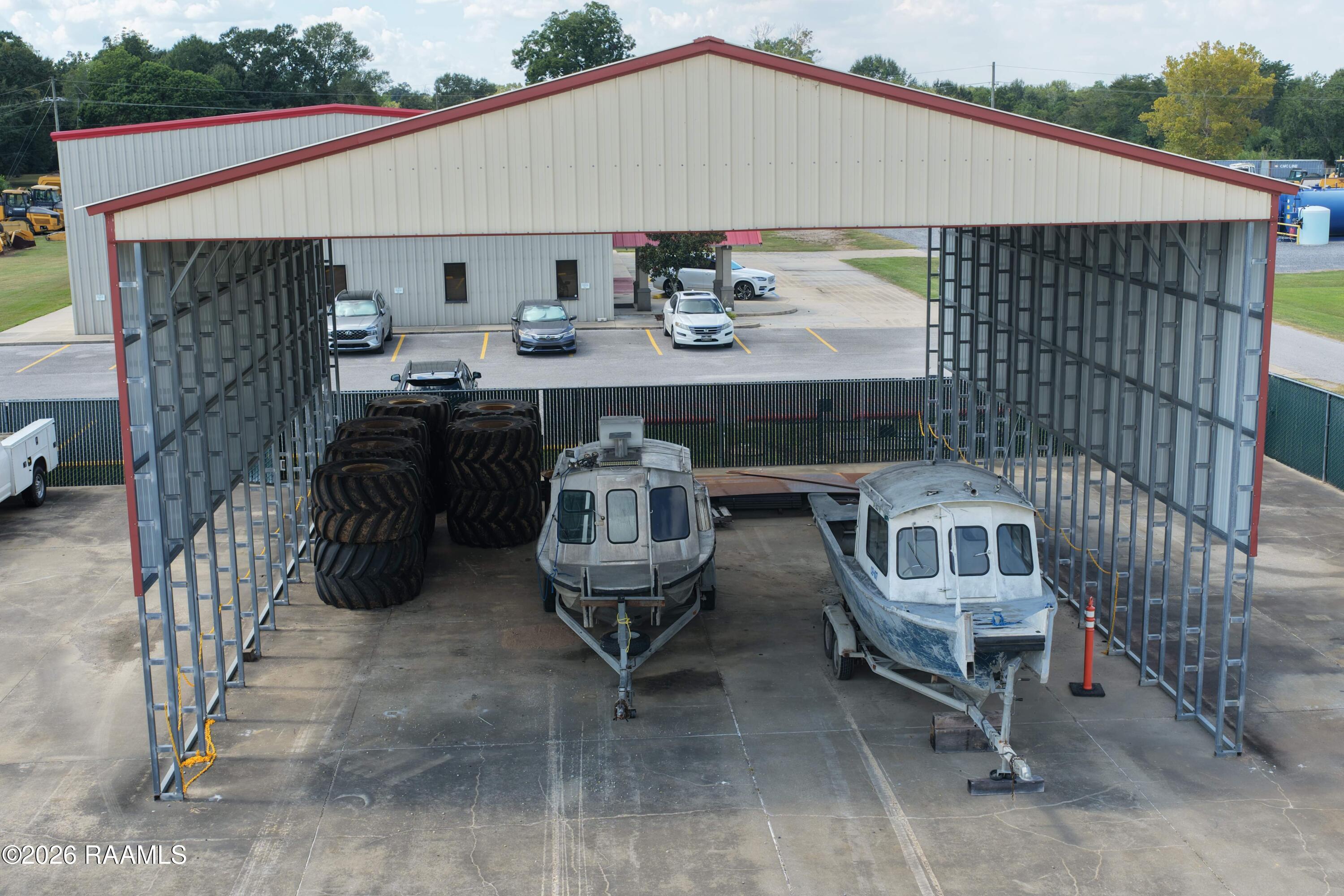 Open-sided metal storage structure shelters two boats on trailers and large tractor tires.