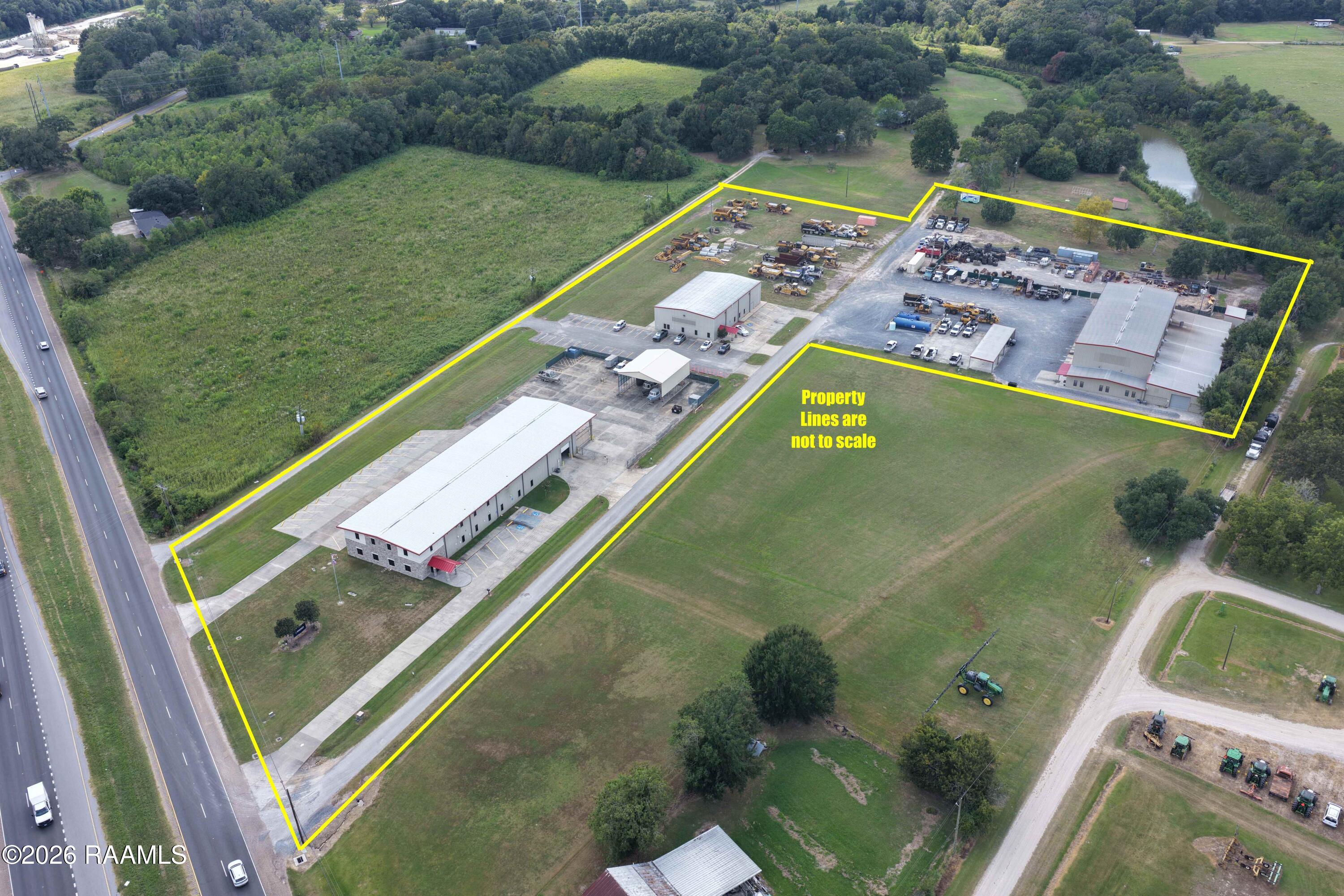 Aerial view of a commercial property outlined in yellow, with several buildings and open land beside a highway.