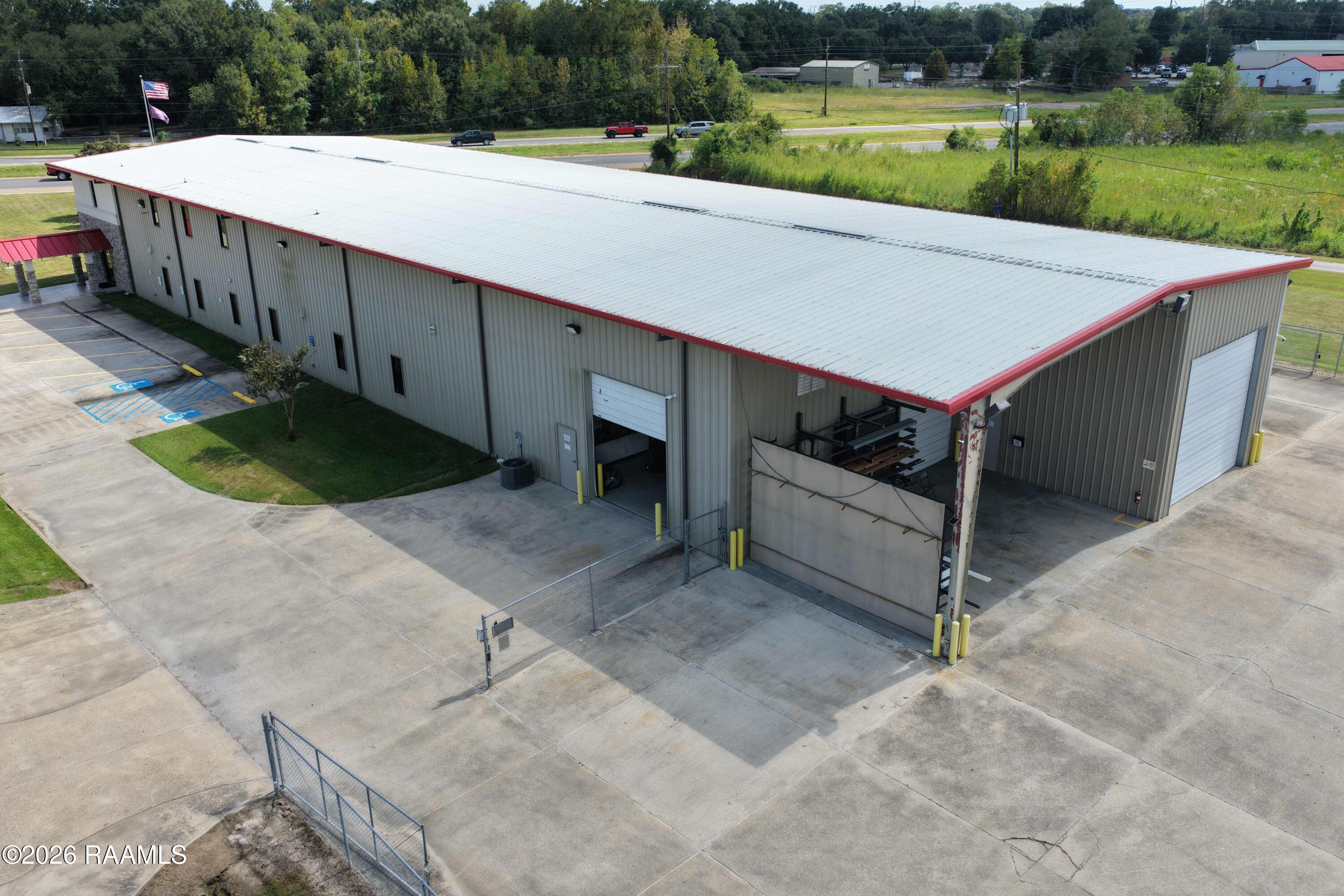 Large gray metal warehouse with a white roof, red trim, and multiple garage doors, viewed from above.