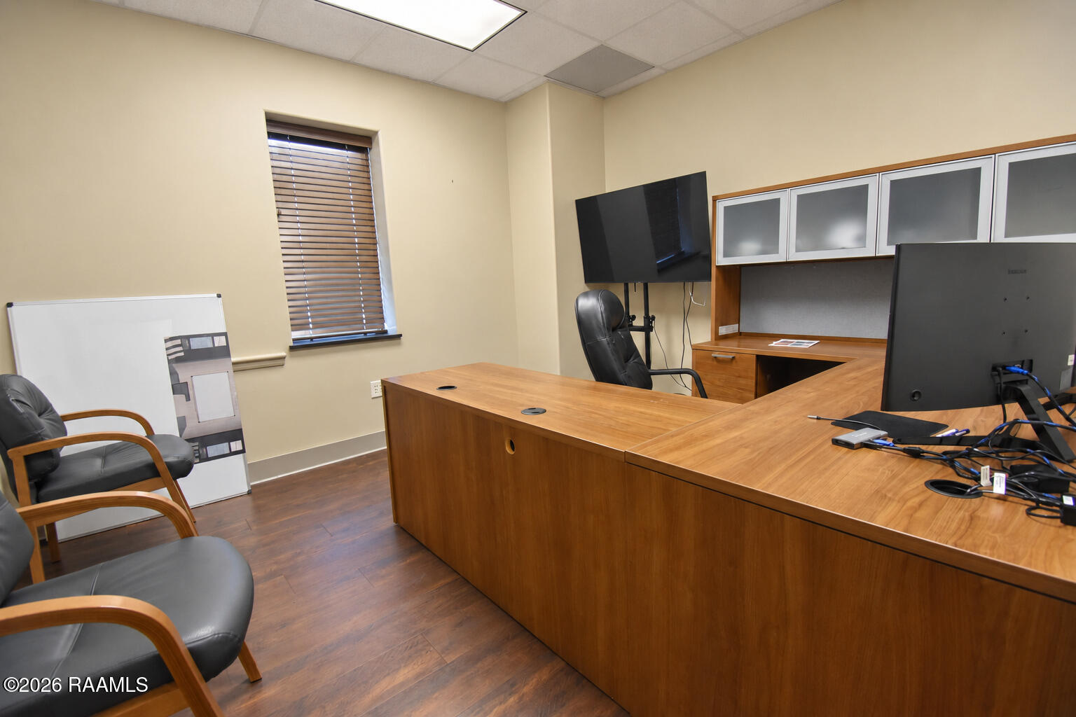 Office with a large wooden desk, wall cabinets, computer monitors, and leather chairs.