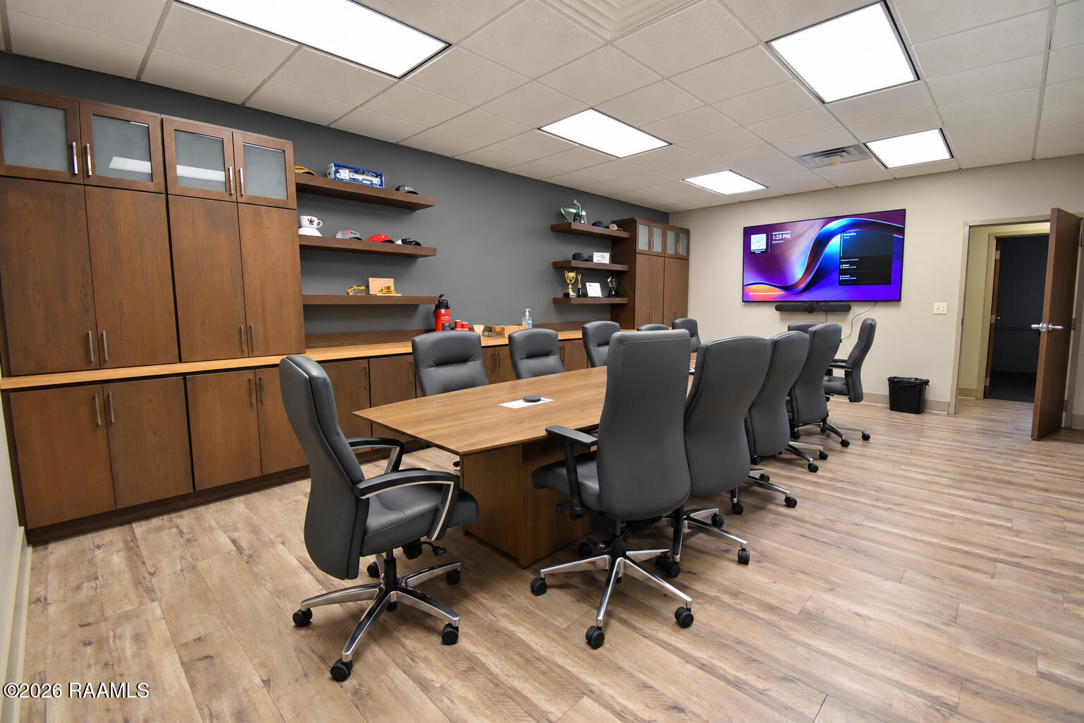 Furnished conference room with a long wood table, black chairs, built-in cabinetry, and a wall-mounted television.