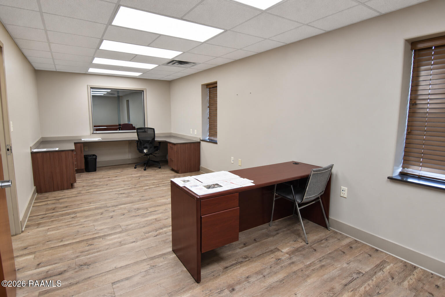 Office interior with two wooden desks, a task chair, and wood-look flooring.