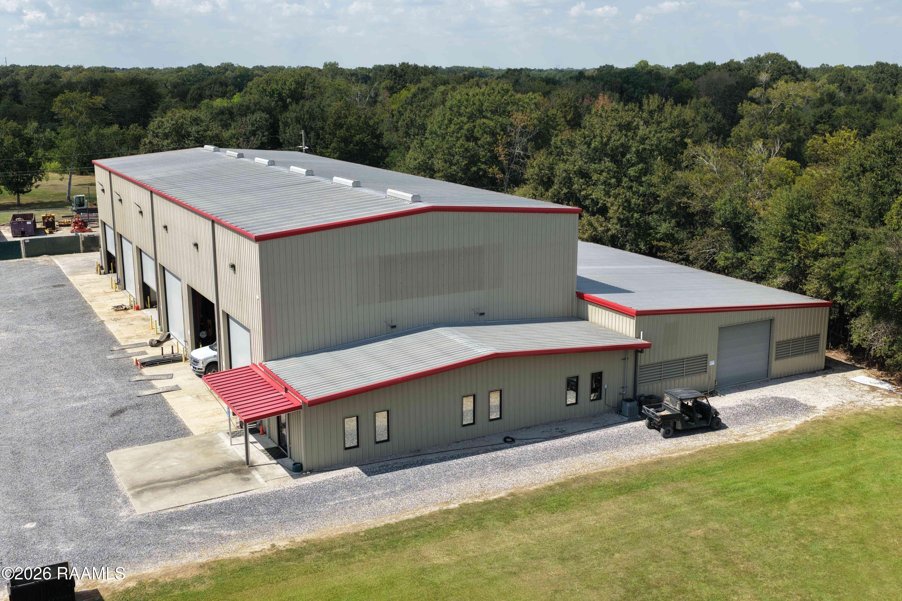 Commercial warehouse with red roof trim, multiple loading-bay doors, and surrounding gravel access area.